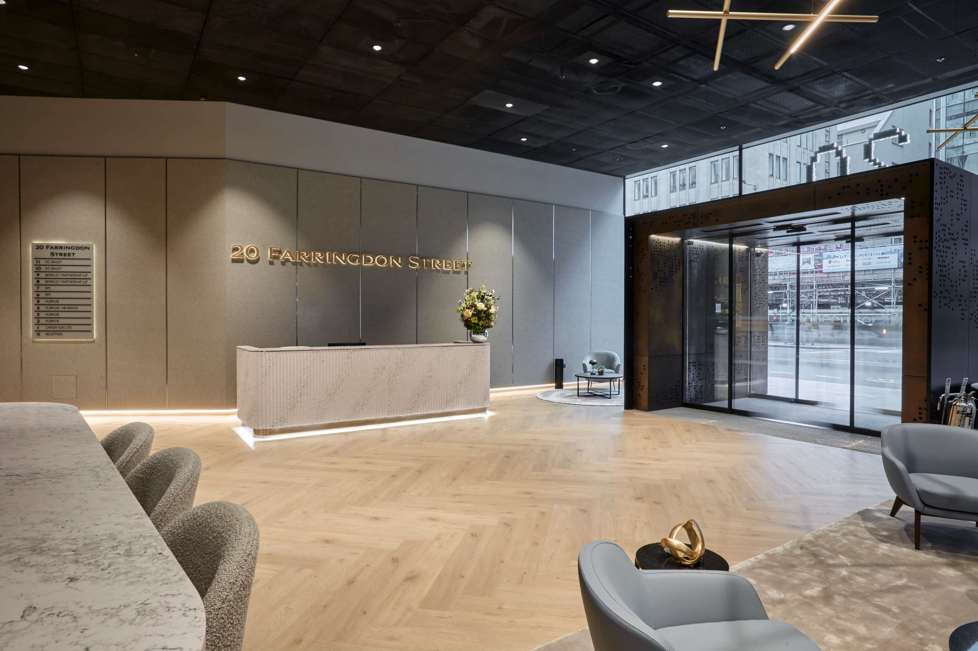 The image shows a modern reception area with a marble front desk, wooden flooring, and large windows revealing an entrance with a glass door.