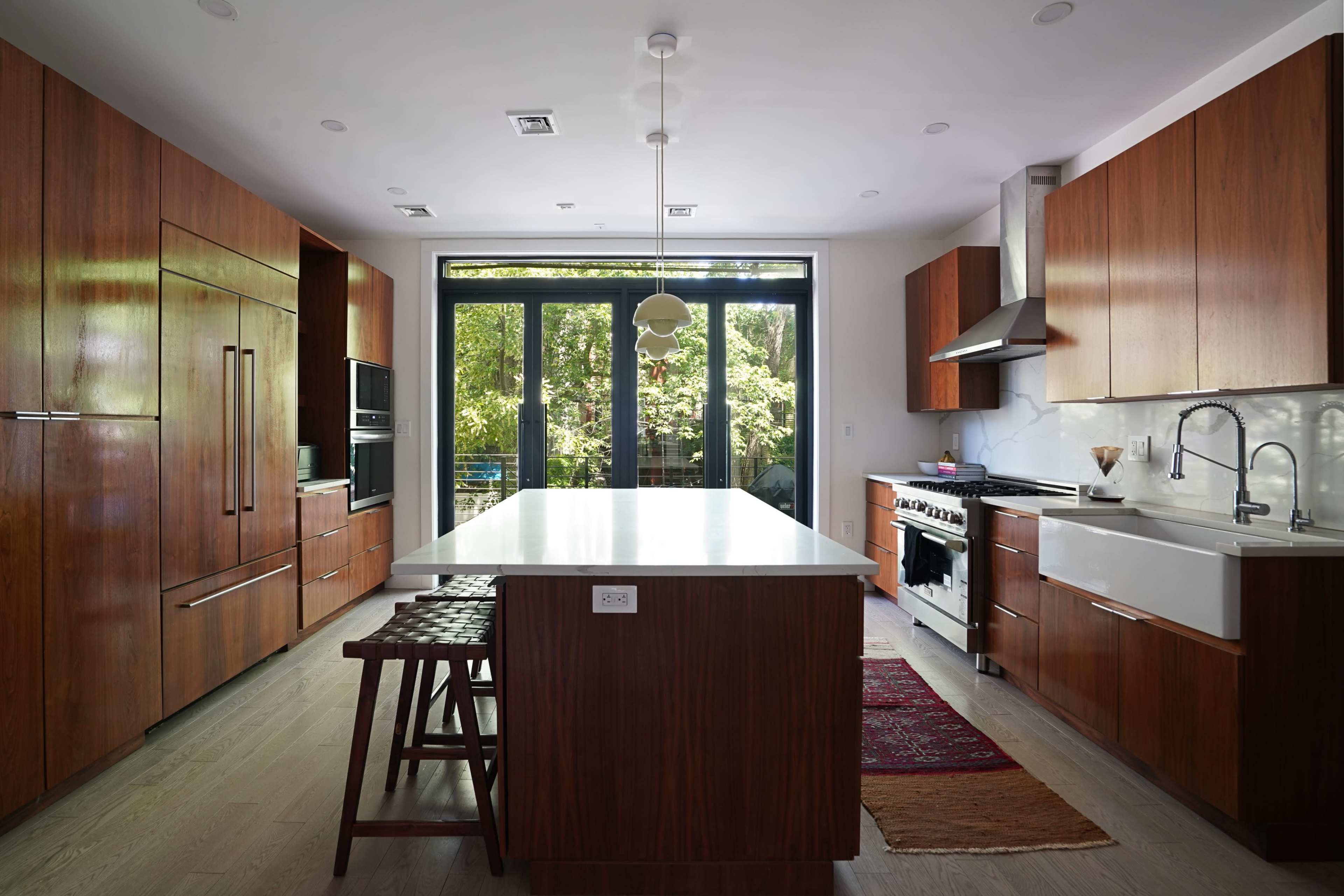 The kitchen features wooden cabinetry, a central island with a white countertop, and large windows that overlook greenery.