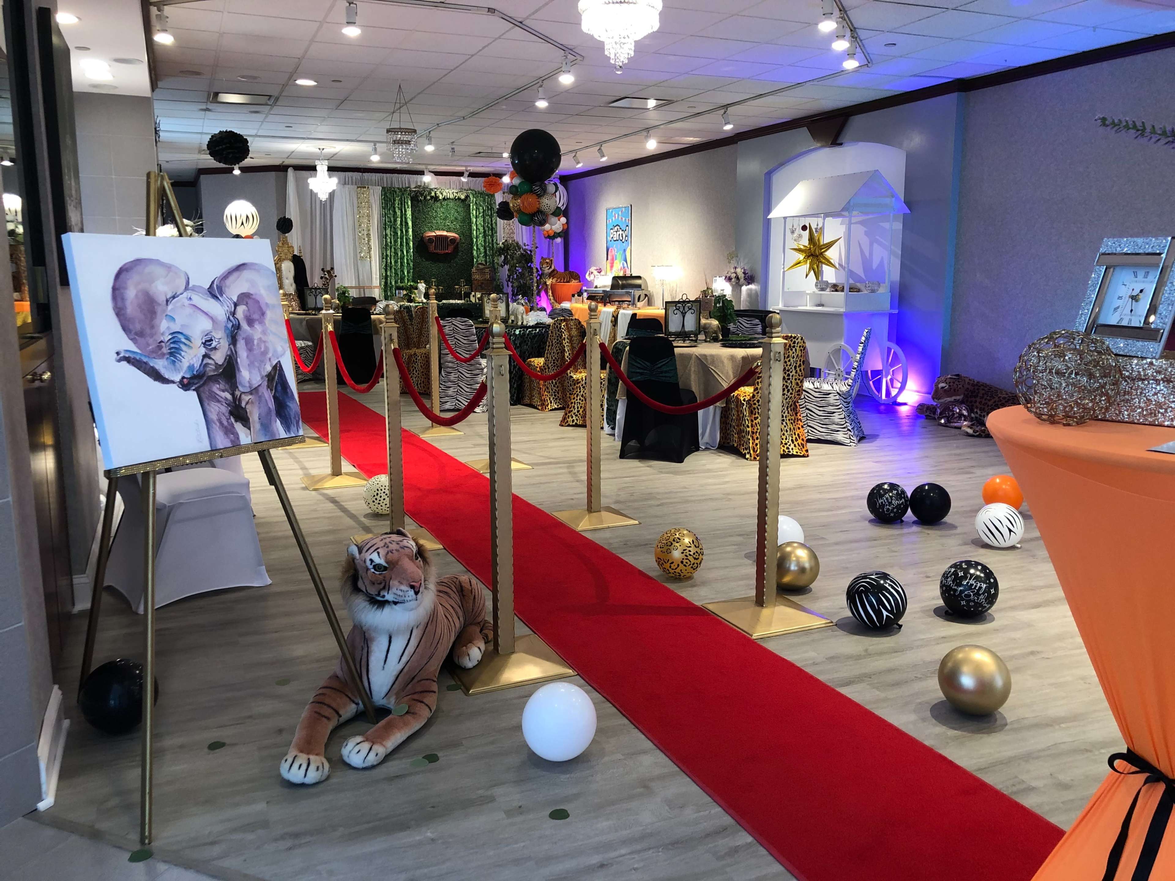 A venue is decorated with a red carpet, animal-themed decor, and an artwork of an elephant displayed on an easel.