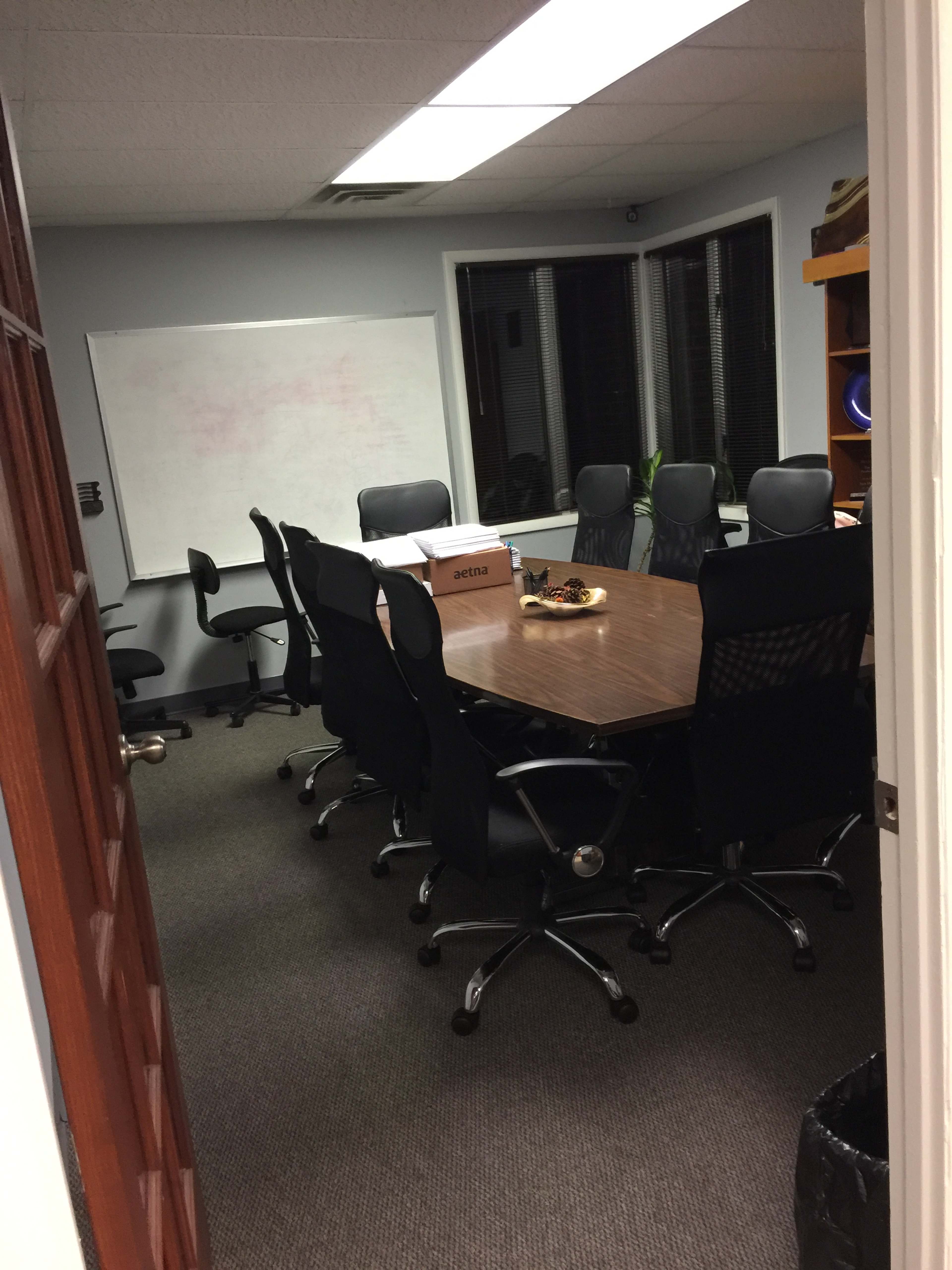 A conference room with a large table surrounded by several office chairs, a whiteboard on the wall, and a box on the table.