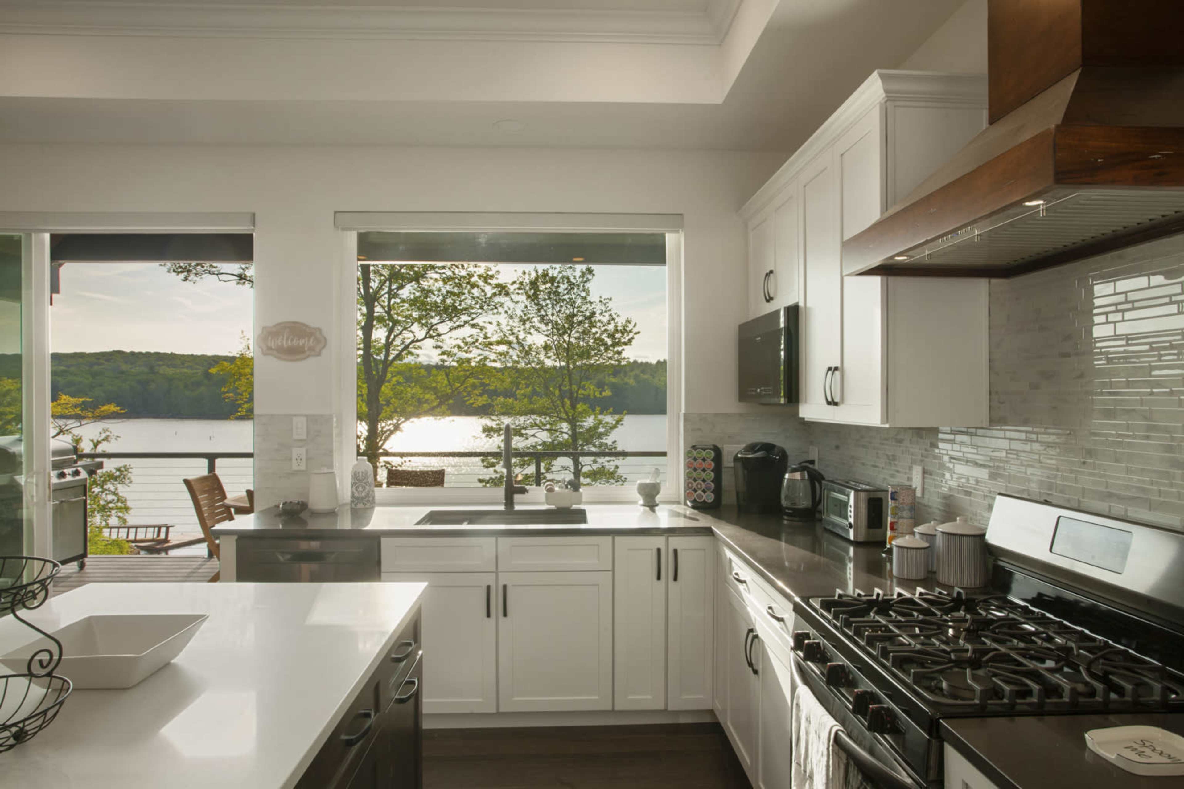 A modern kitchen features white cabinets, a stainless steel gas stove, and a view of a lake through large windows.