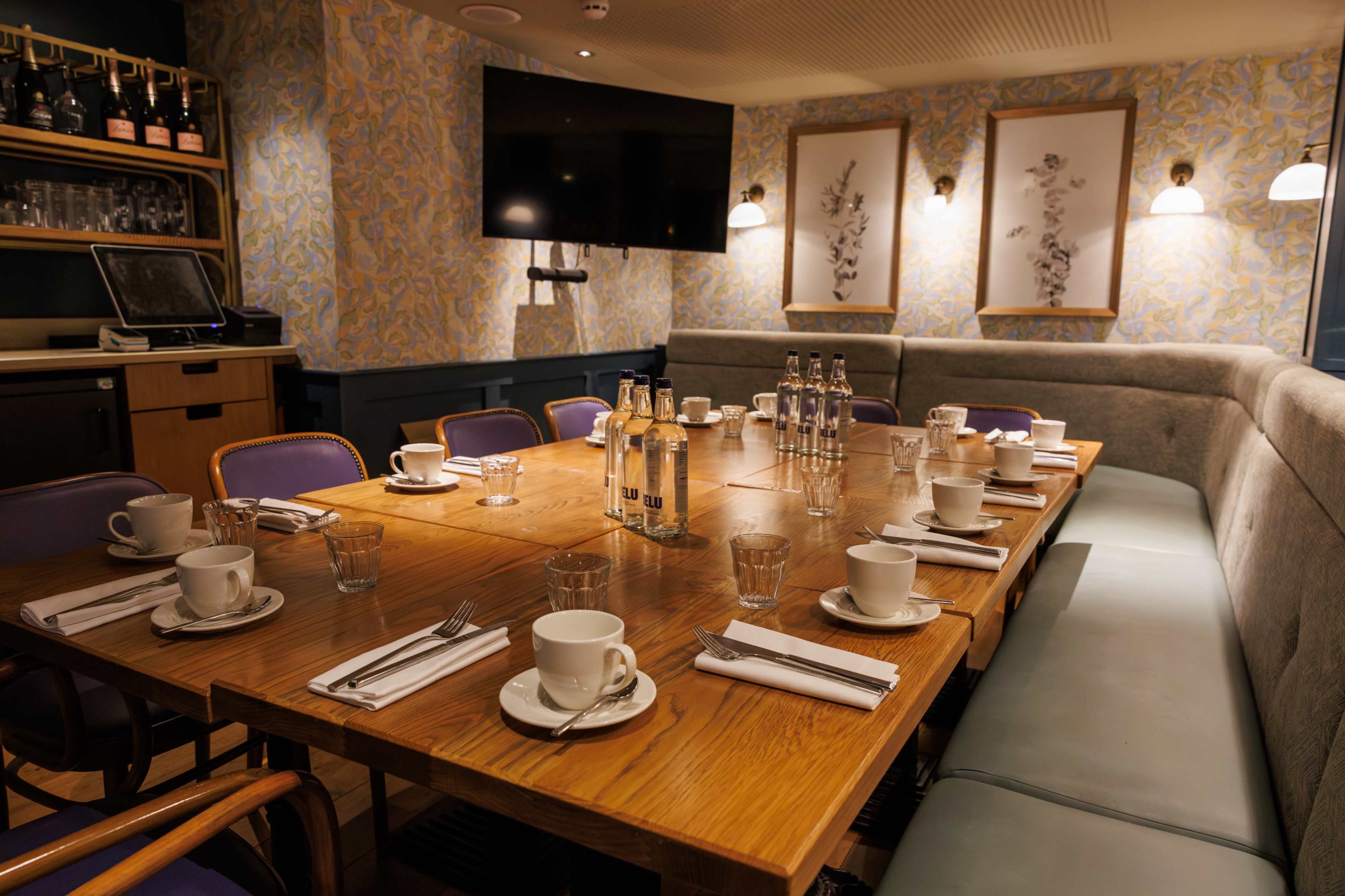 A dining table is set with cups, glasses, and cutlery in a cozy, well-decorated private room.
