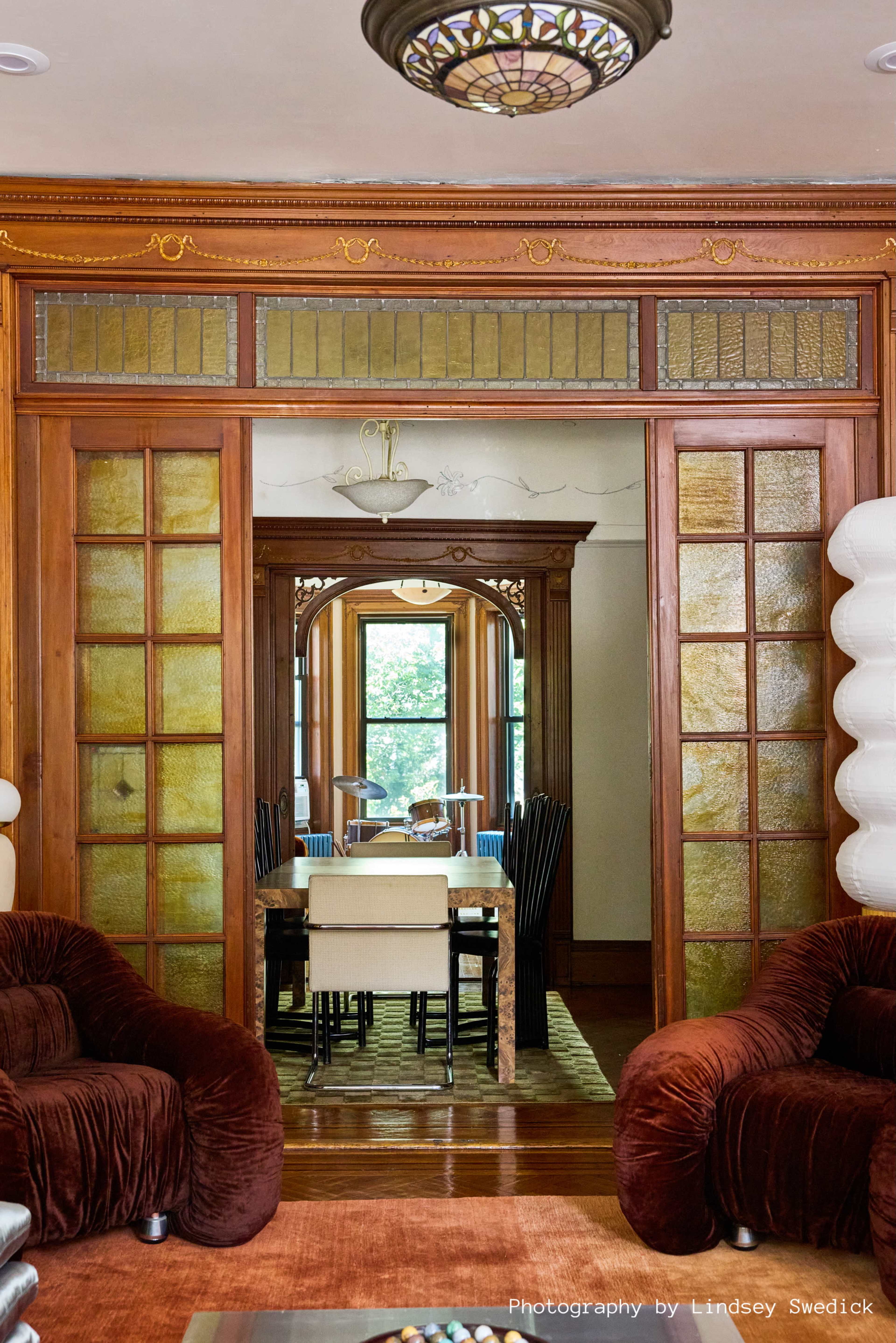 The image shows a spacious interior featuring a dining area with a wooden table and black chairs, framed by glass panelled doors and surrounded by rich wooden details.
