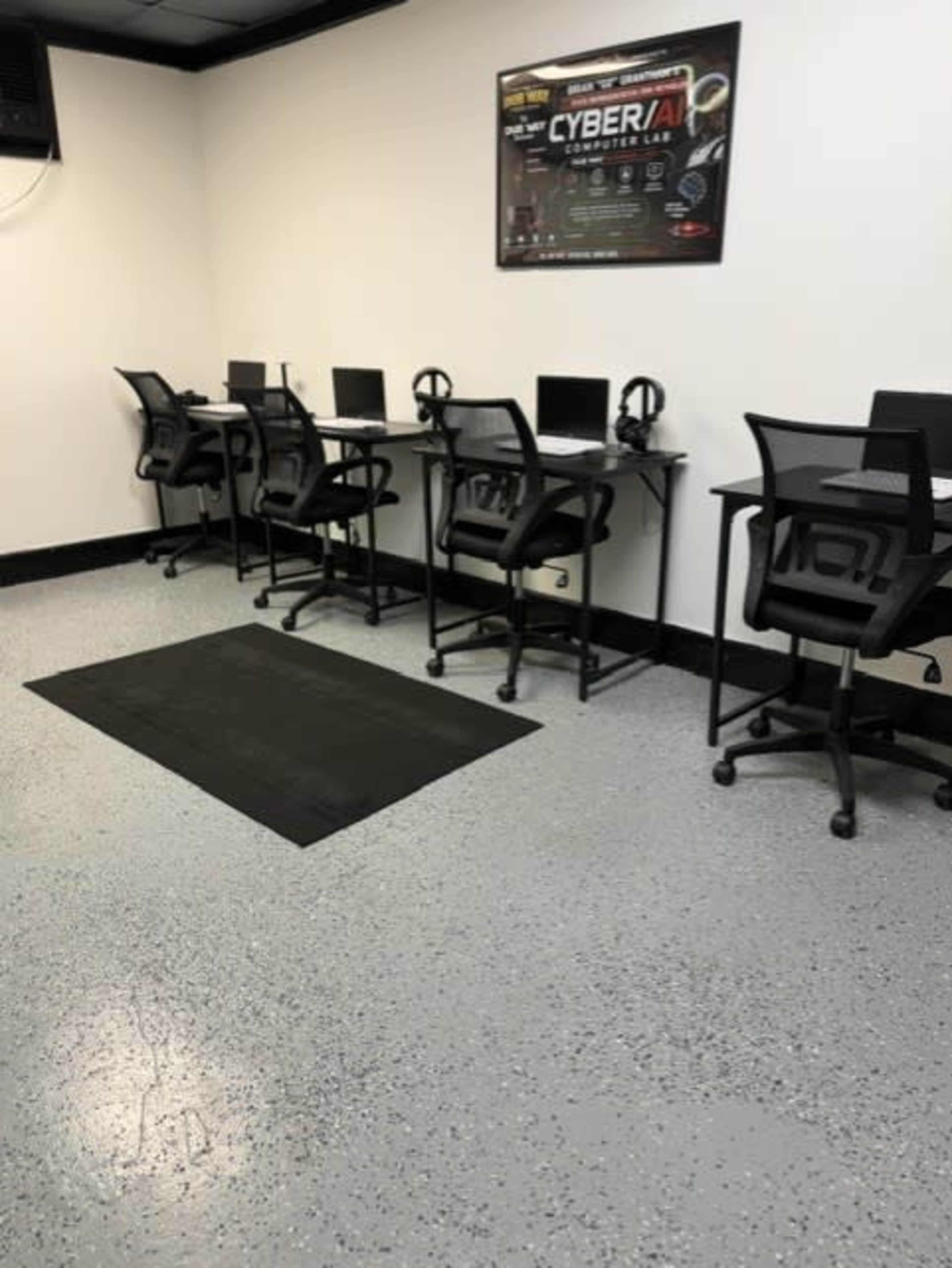 The image shows a clean, empty computer lab with several desks equipped with monitors, headphones, and rolling chairs.