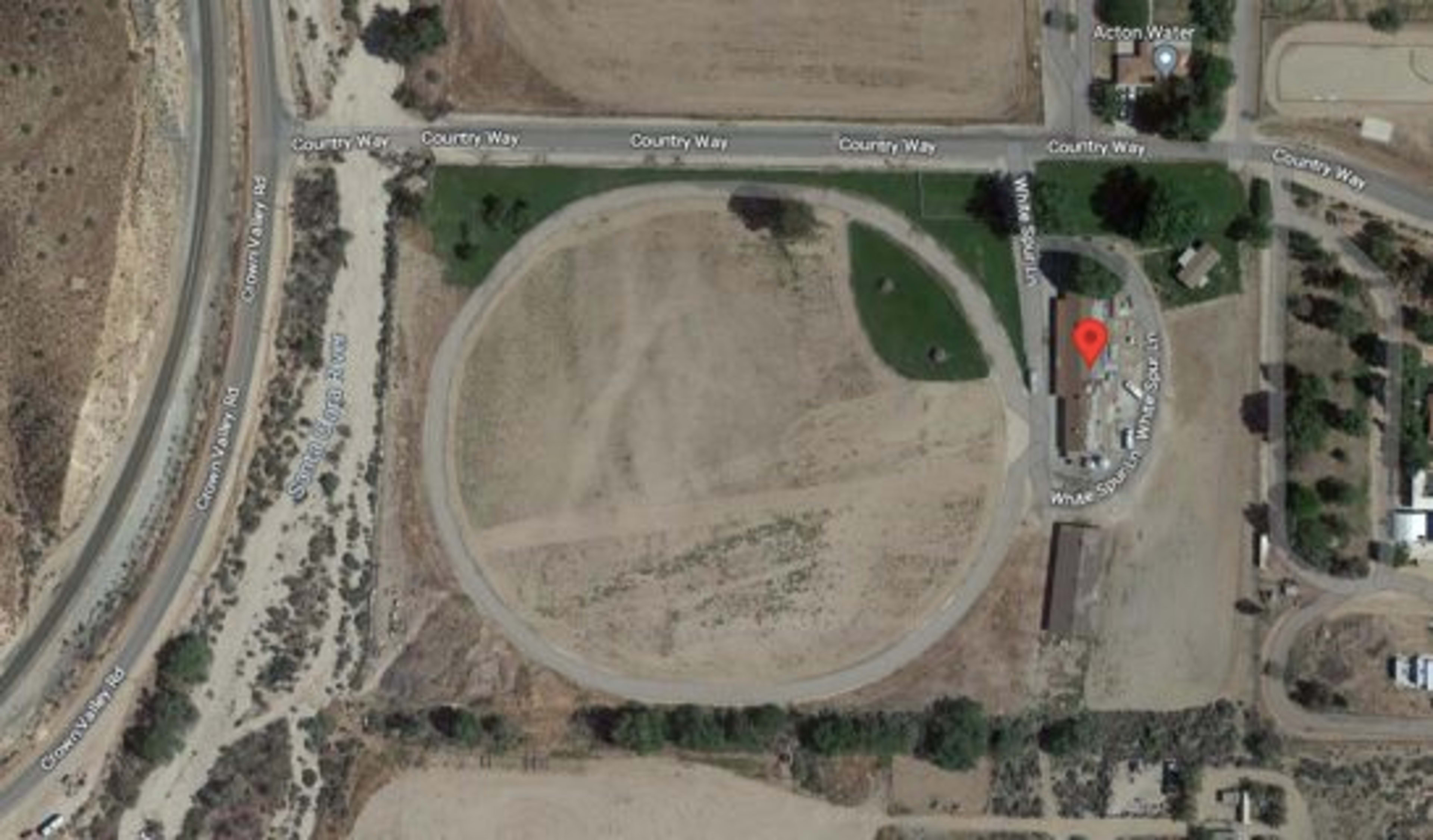 An aerial view of a circular dirt track surrounded by roads named Country Way and Acton Water.
