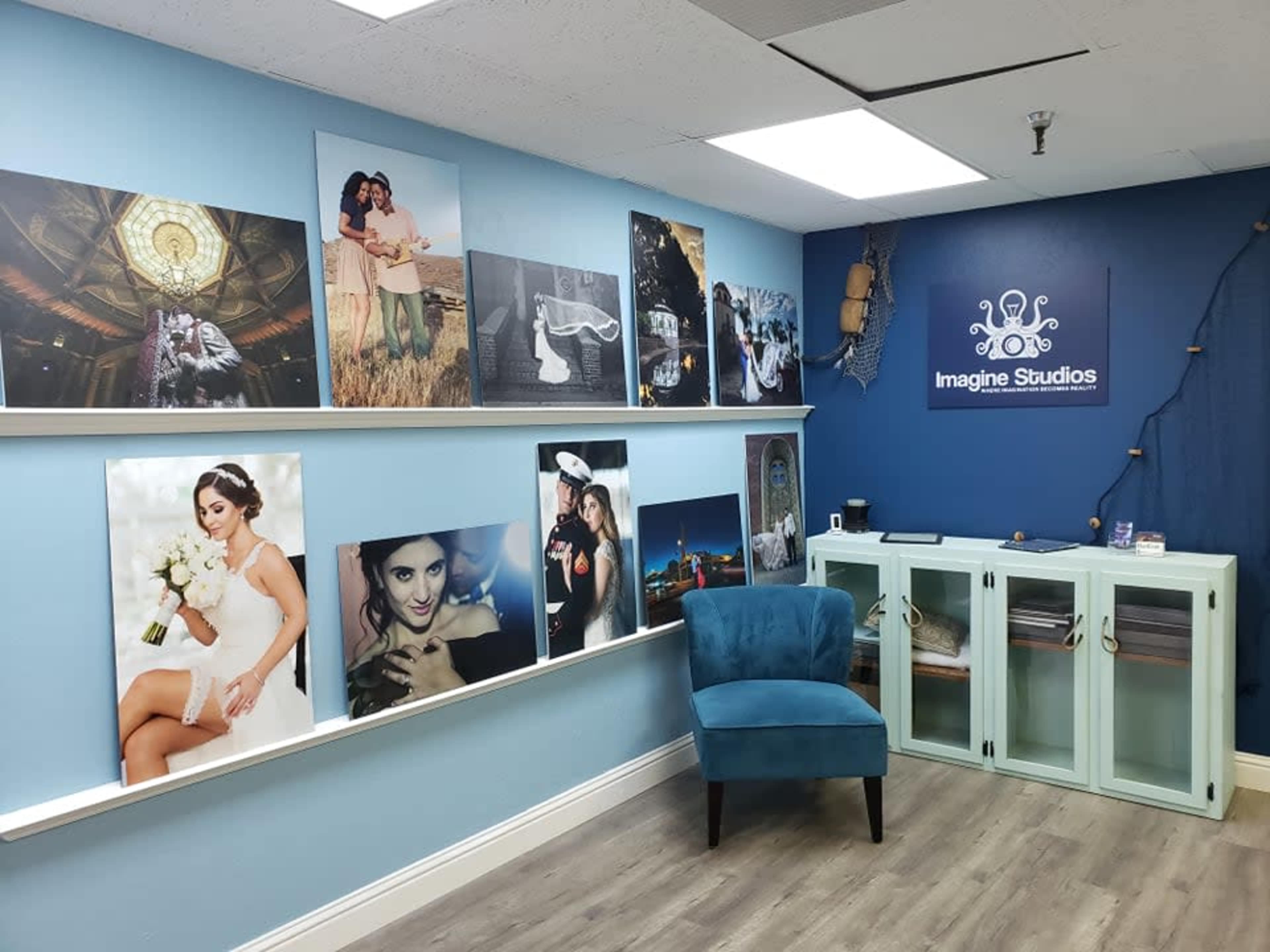 A blue-walled studio gallery featuring framed photographs, a chair, and a display cabinet.