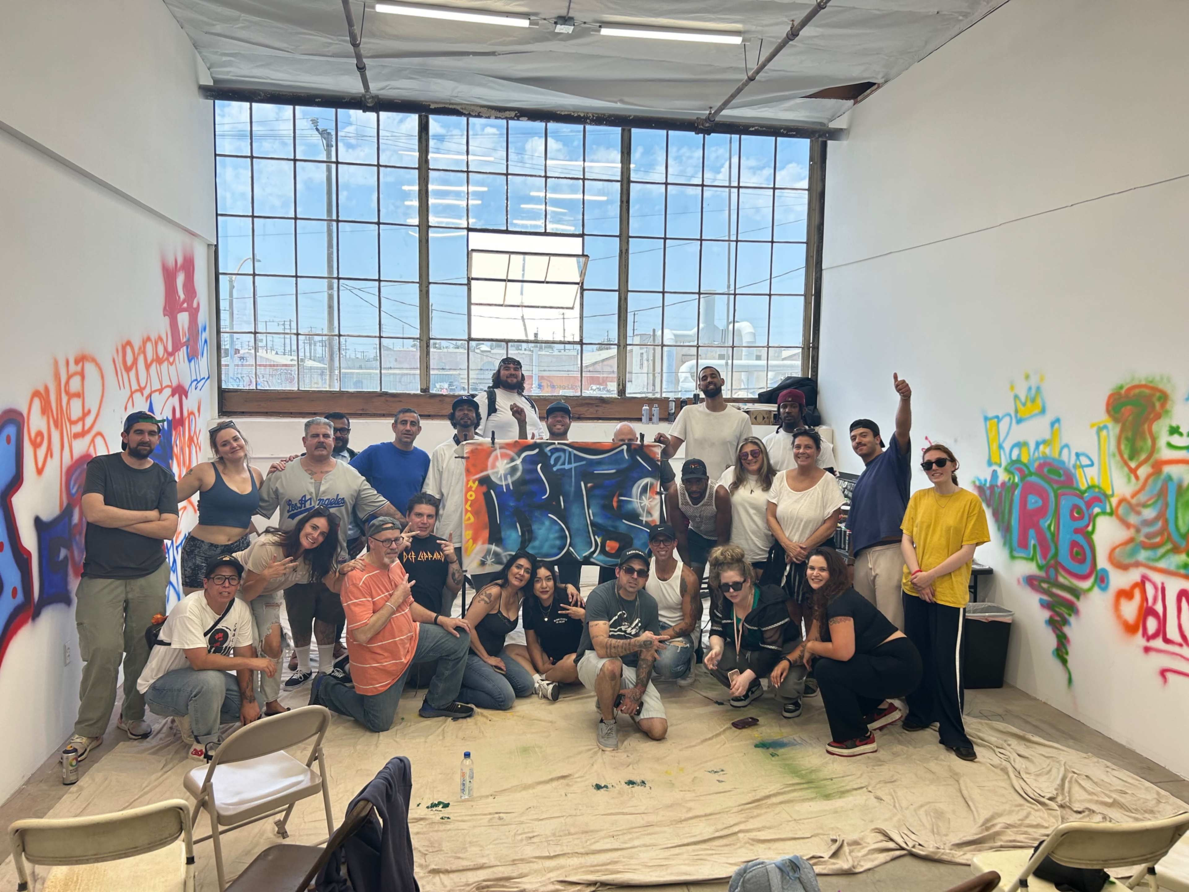 A diverse group of individuals poses together in a brightly lit room adorned with graffiti on the walls.