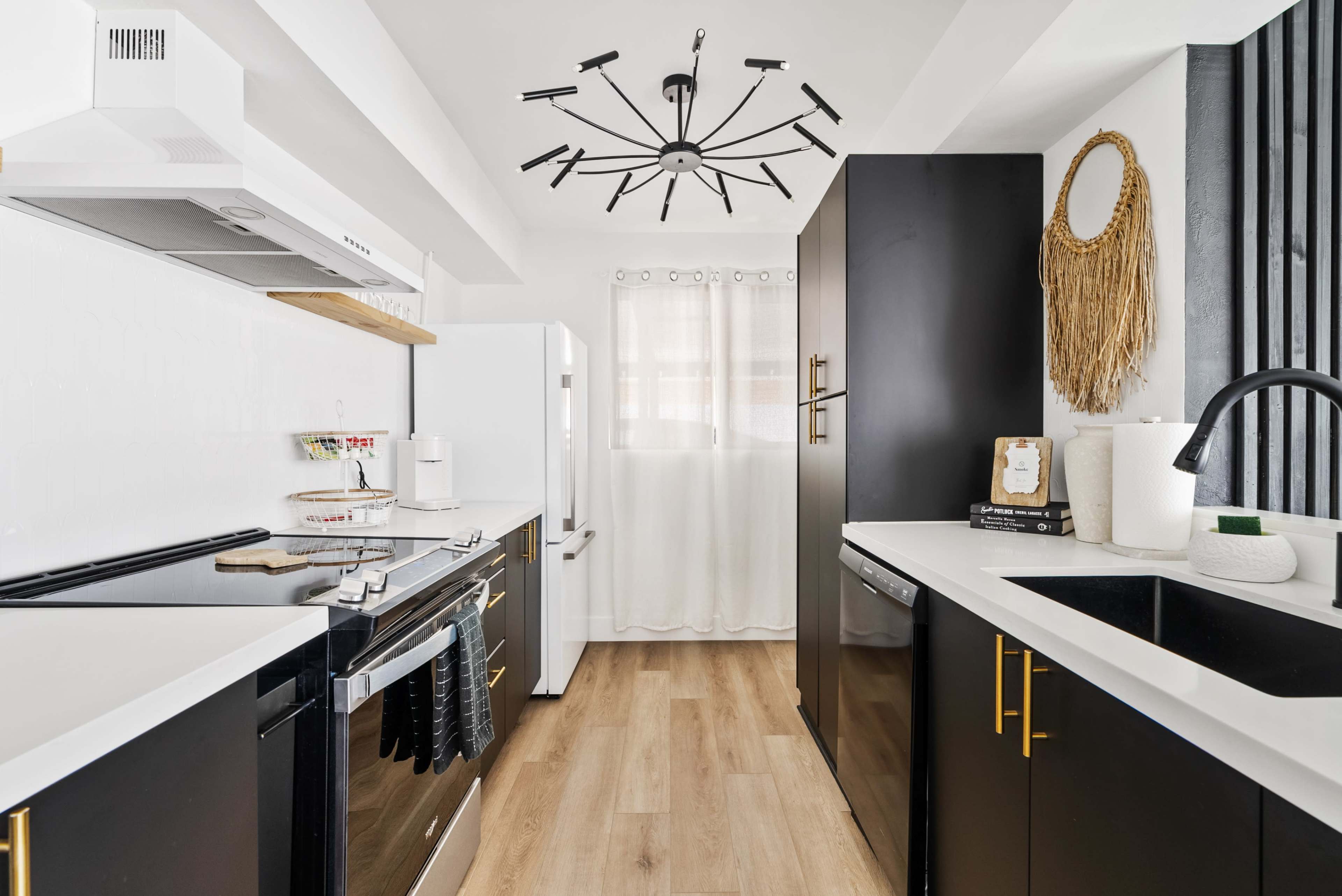 The kitchen features black cabinetry, stainless steel appliances, and a modern chandelier, with a white curtain allowing light to enter.