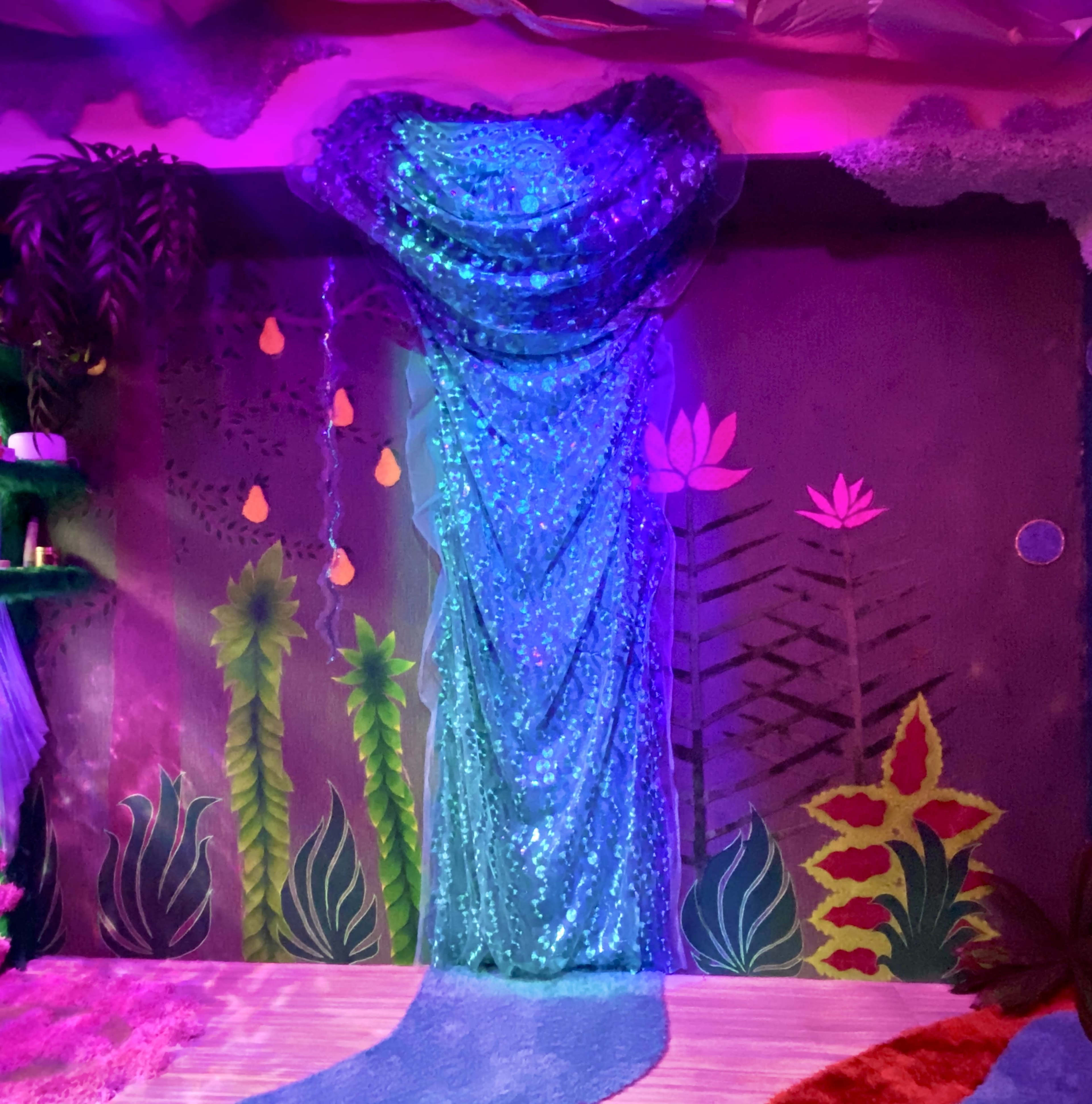 The image shows a vibrant mural depicting aquatic plants and flowers, complemented by a sequined curtain in shades of blue hanging on a wall.