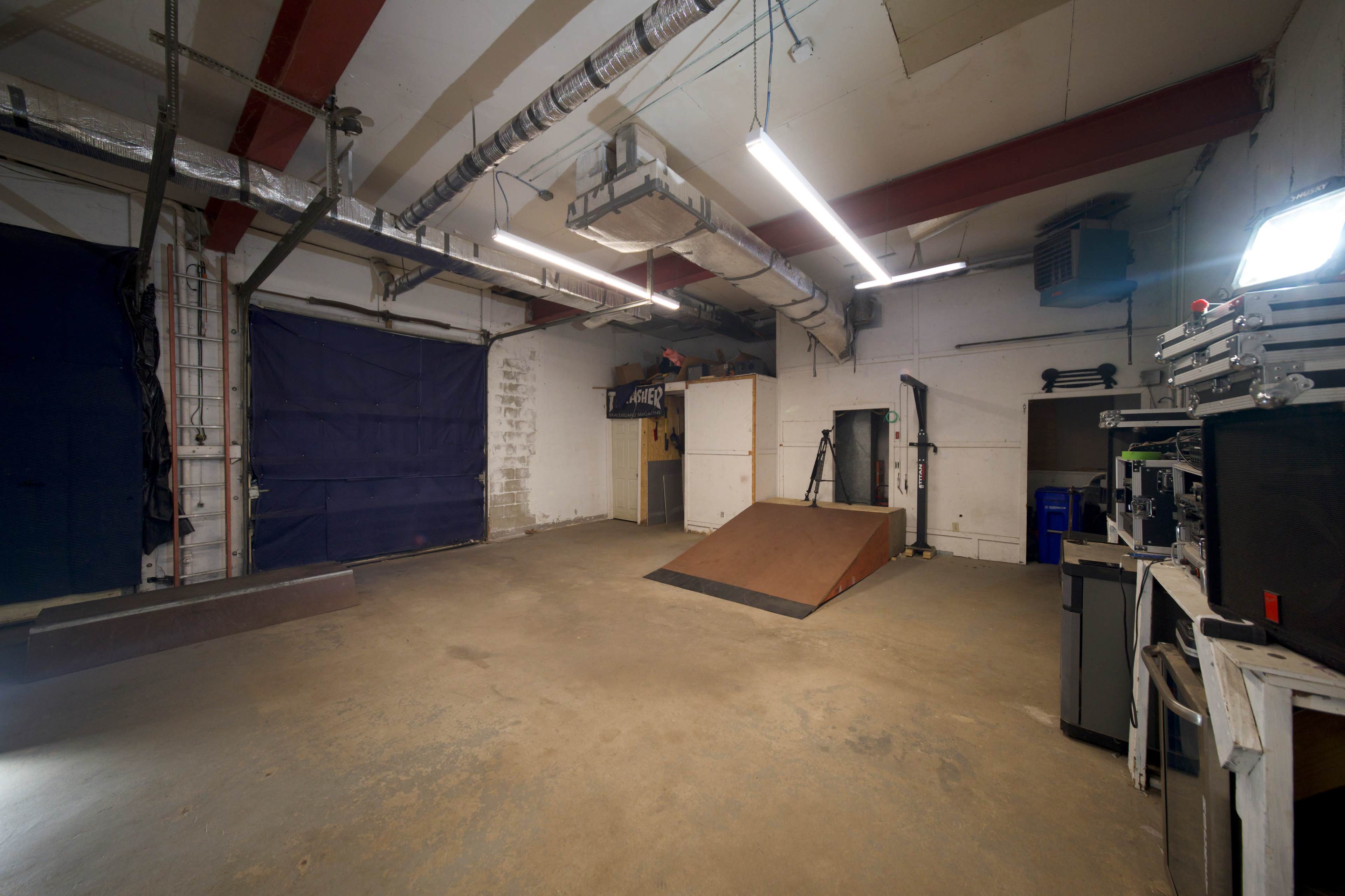 An indoor skatepark with a wooden ramp and various equipment lined up against the walls.