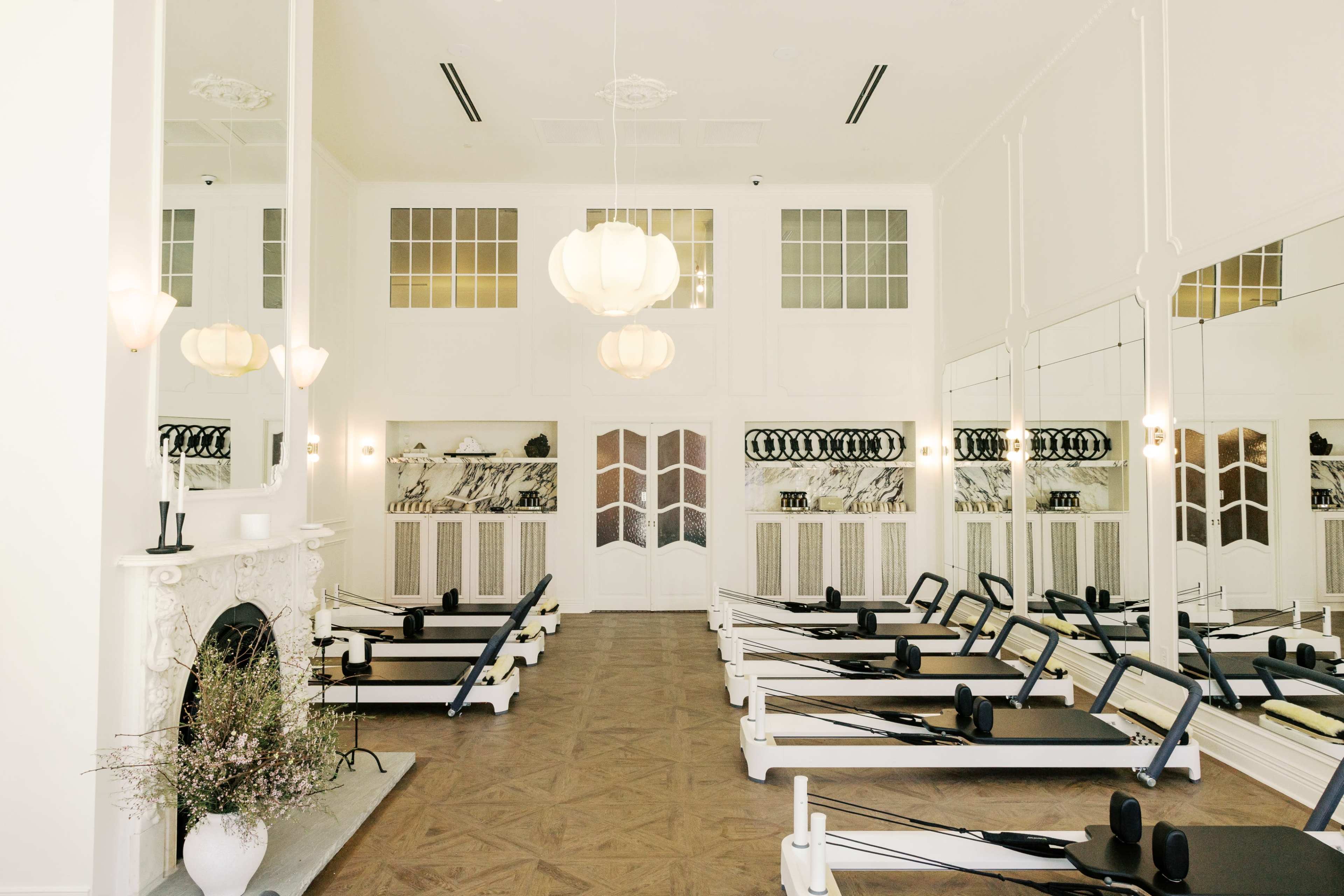 The image shows a spacious, elegantly designed fitness studio with several rowers arranged neatly in rows, alongside large mirrors and soft lighting fixtures.