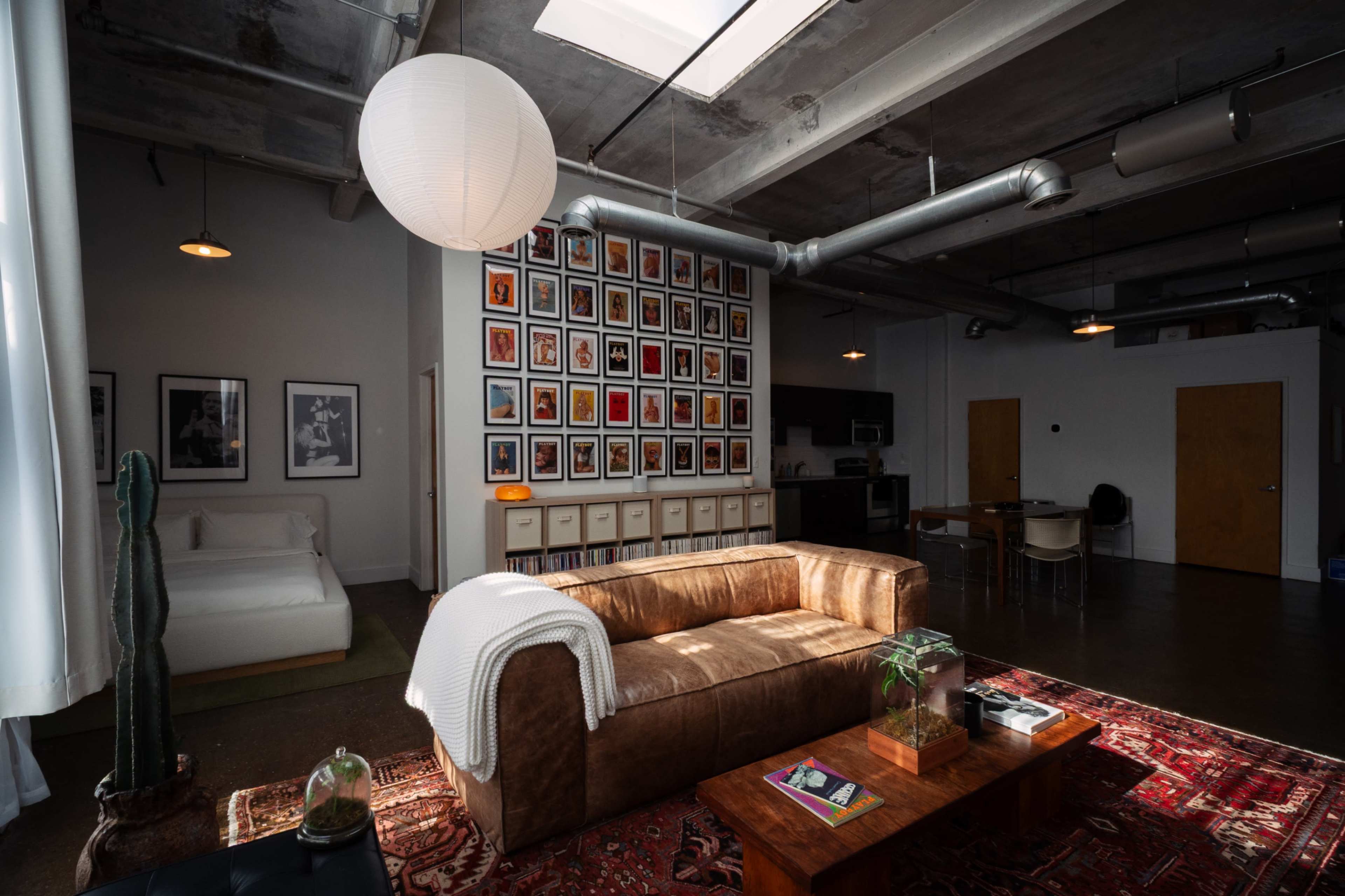 A spacious studio apartment features a leather couch, a gallery wall of framed photos, and a dining area with modern furnishings.