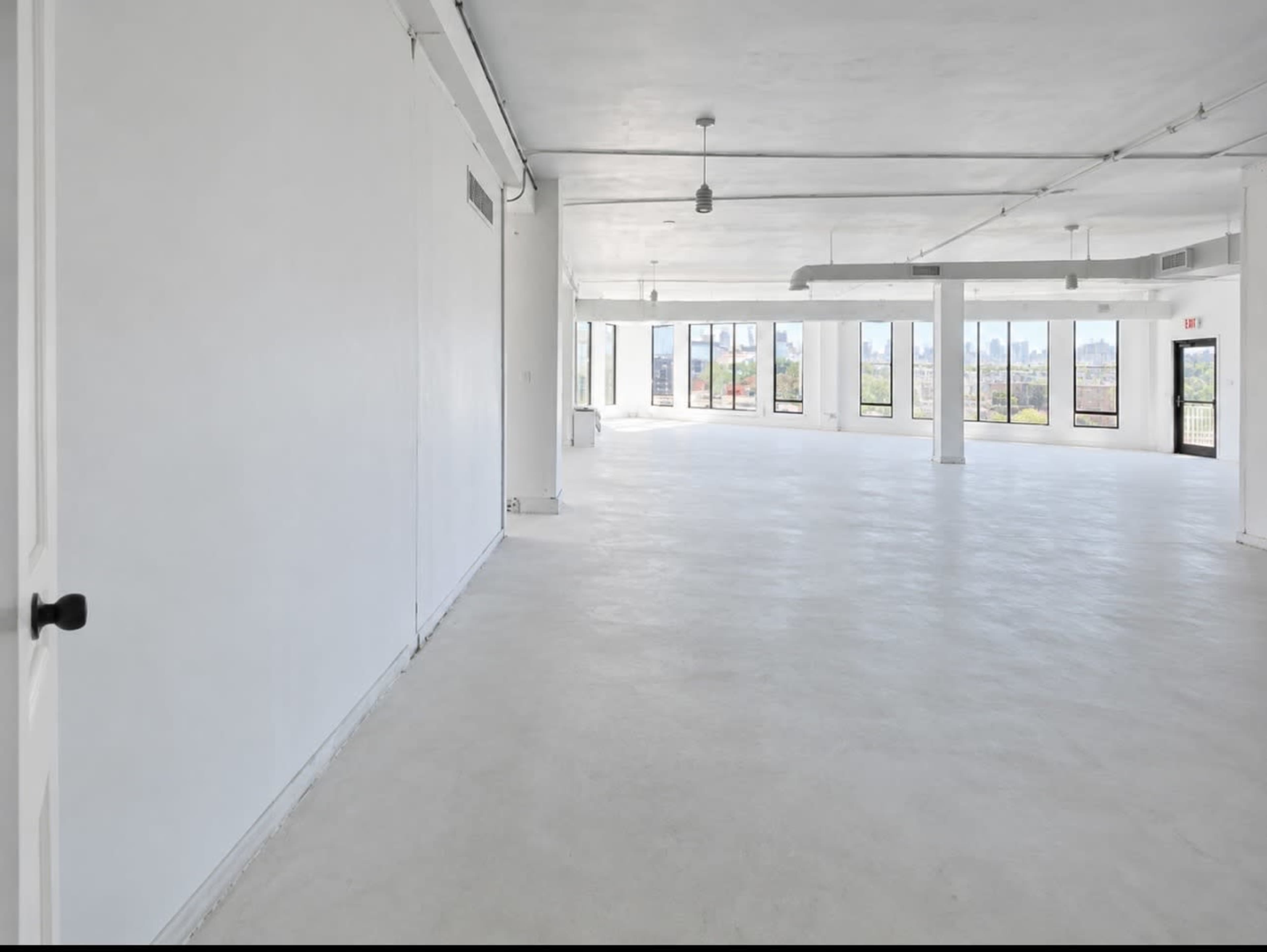 The image shows a spacious, empty room with white walls and large windows that allow natural light to enter.