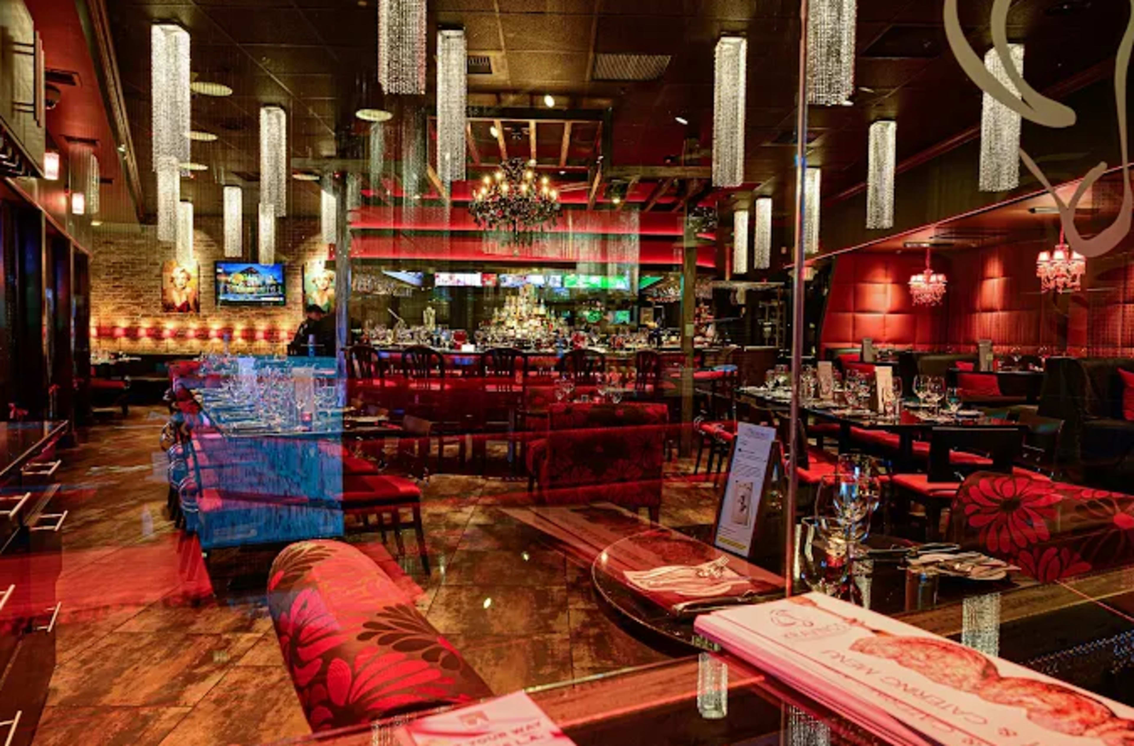The image shows an upscale restaurant interior featuring red decor, elegant chandeliers, and tables set with fine dining arrangements.