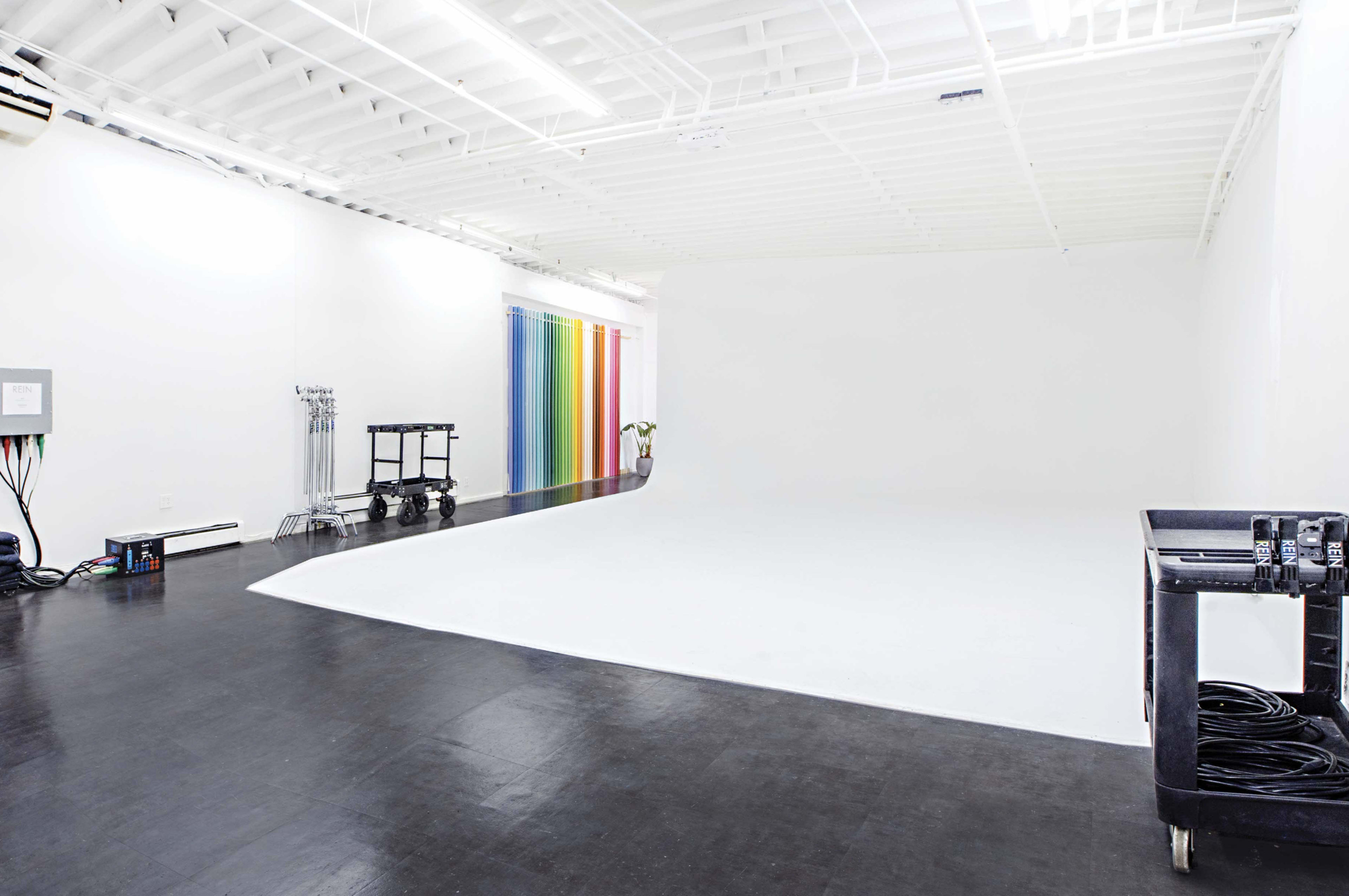 A spacious, well-lit studio with a white backdrop, colorful curtain, and equipment carts along the walls.
