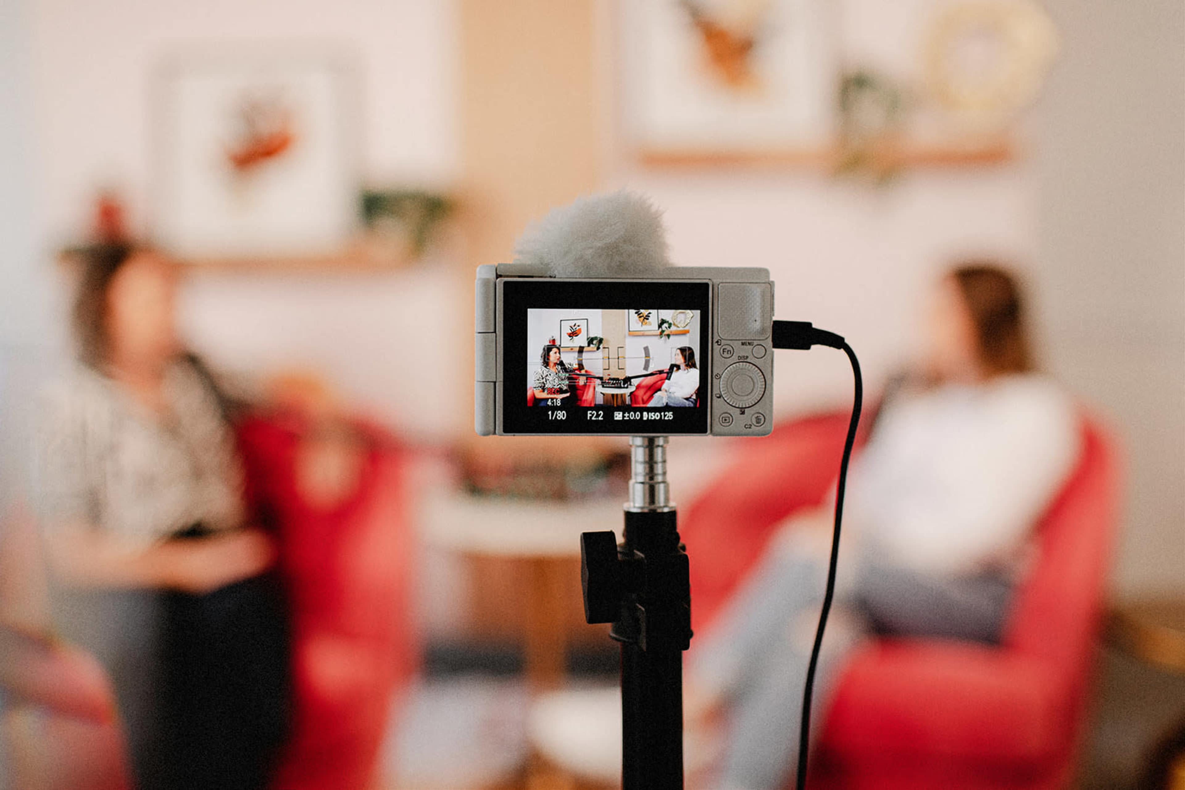 A camera on a tripod focused on two people seated on a red sofa in a conversation.