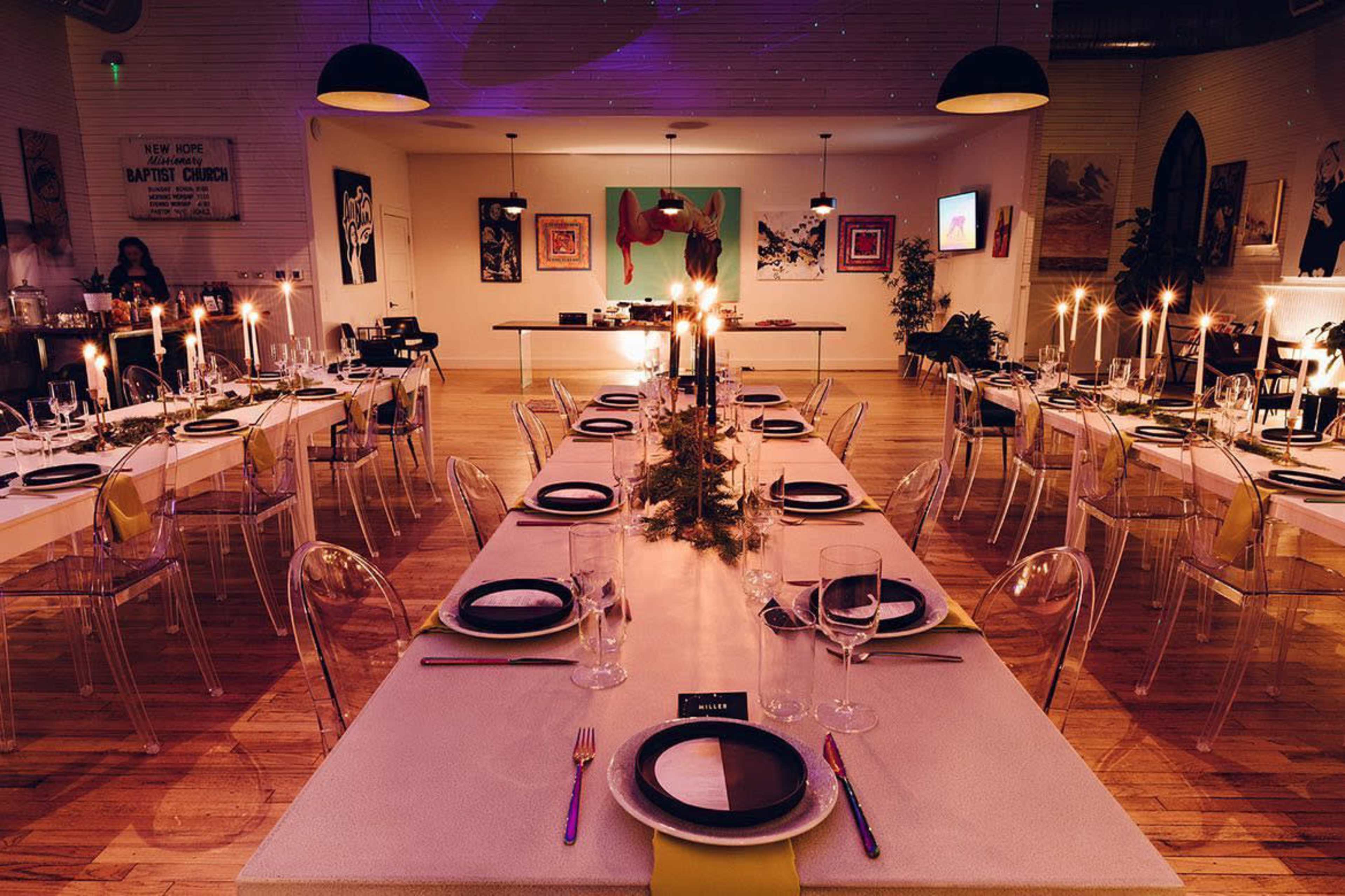A long, elegantly set dining table is arranged with candles and tableware in a stylish restaurant space.