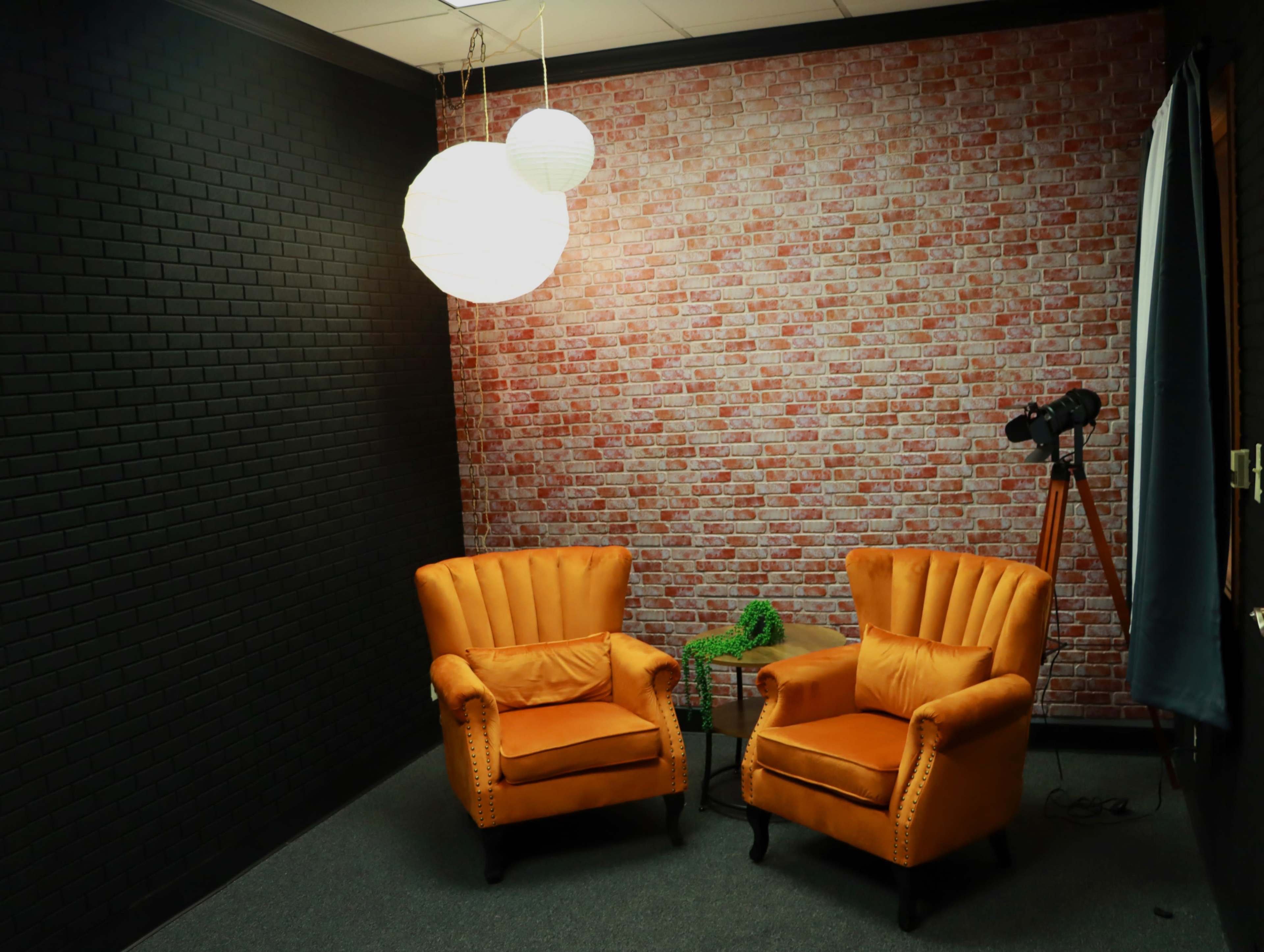 The image shows two orange armchairs facing each other in a room with a brick-patterned wall and a telescope in the corner.