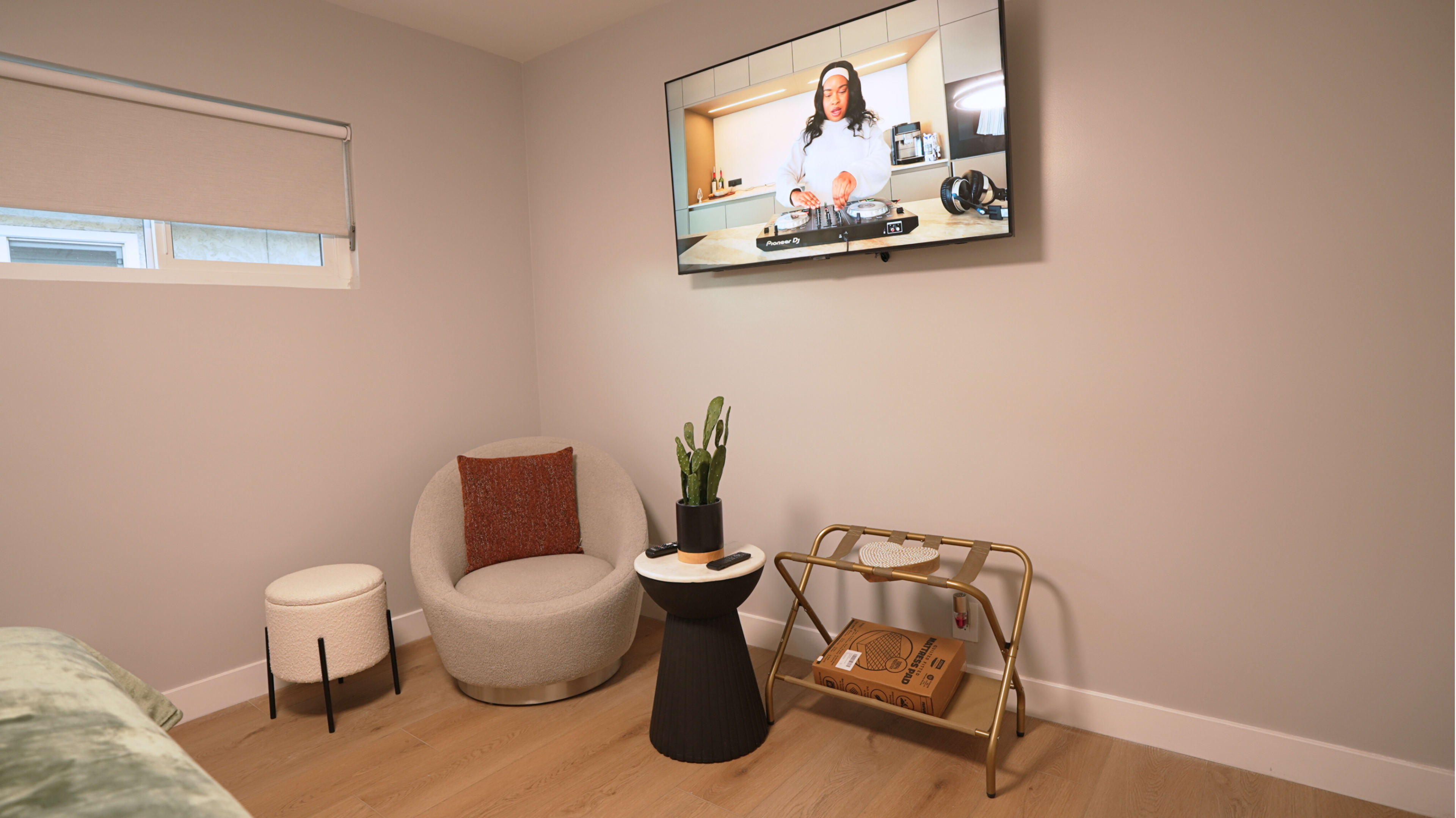 The image shows a modern room with a chair, small table, and a television mounted on the wall displaying a cooking program.