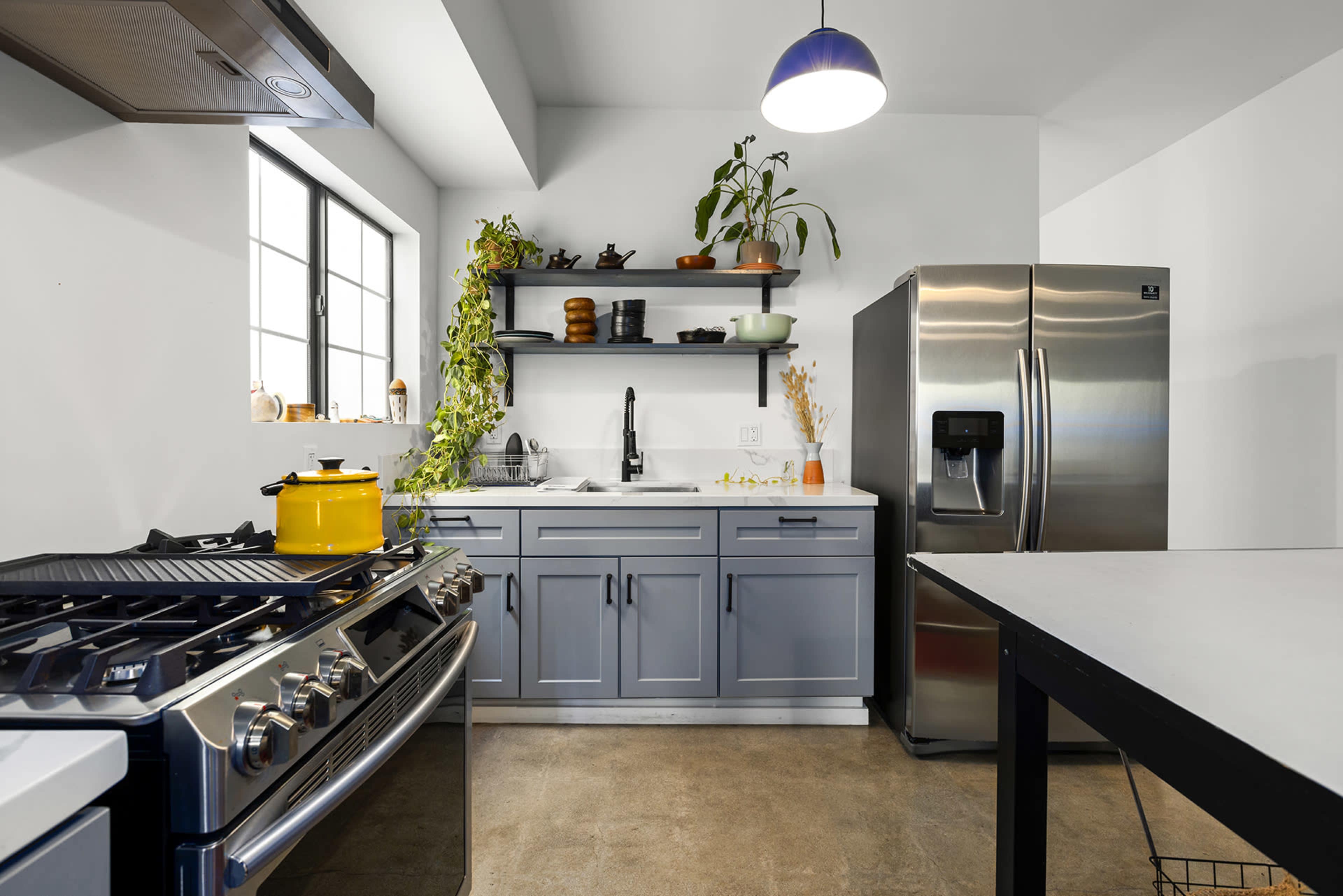 A modern kitchen features gray cabinetry, a stainless steel refrigerator, and a gas stove with a yellow pot on the counter.