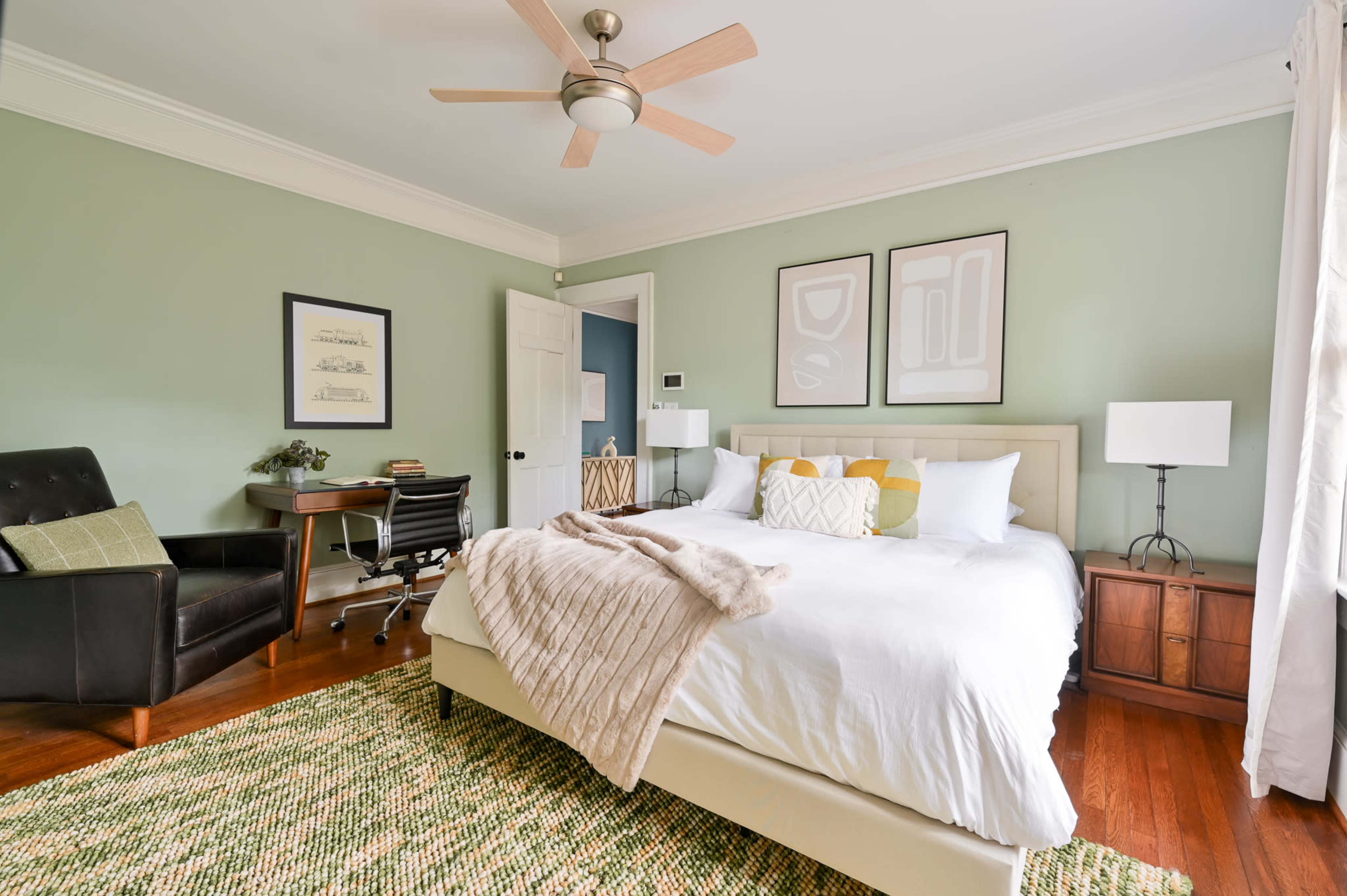 The bedroom features a bed with white linens, a desk with a chair, and light green walls.