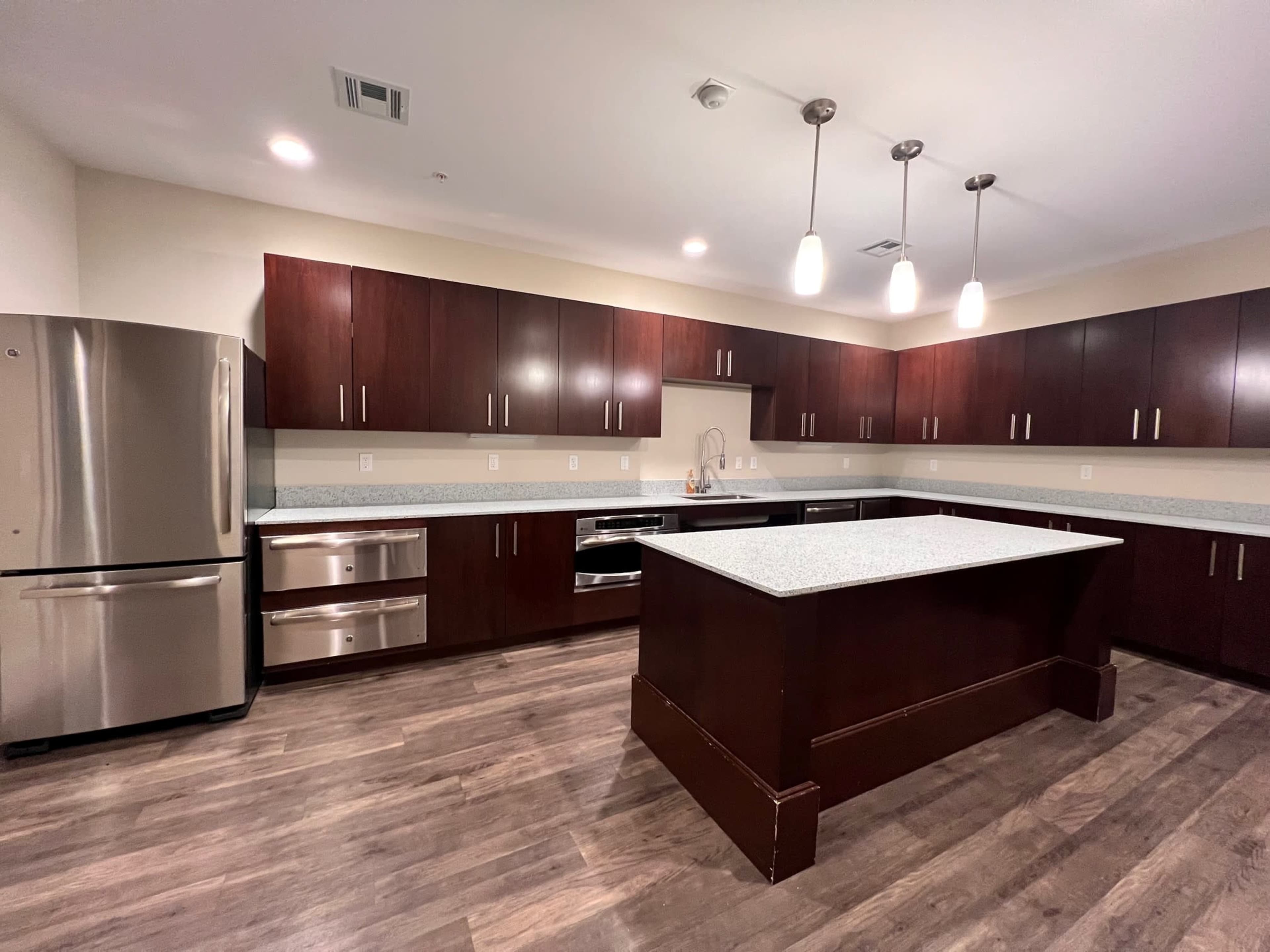 A spacious kitchen with dark wood cabinets, a large island, and stainless steel appliances, including a refrigerator and oven.