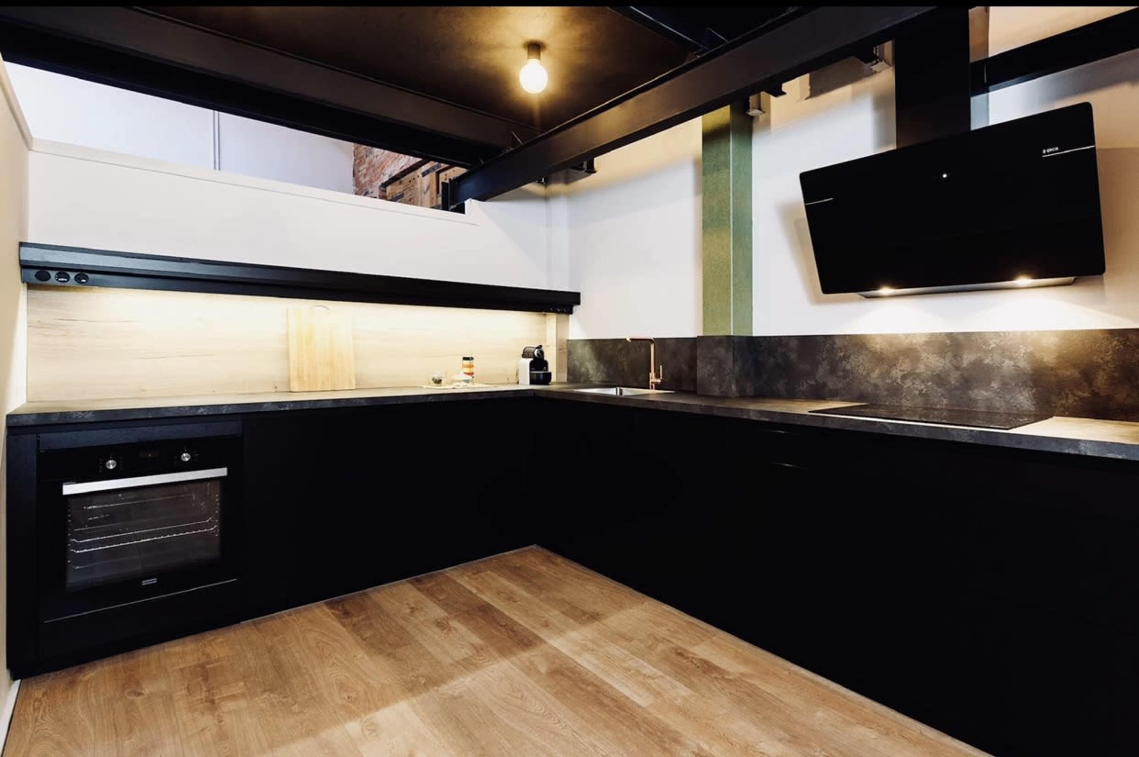 A modern kitchen with dark cabinetry, a built-in oven, and under-cabinet lighting on a light-colored wall.