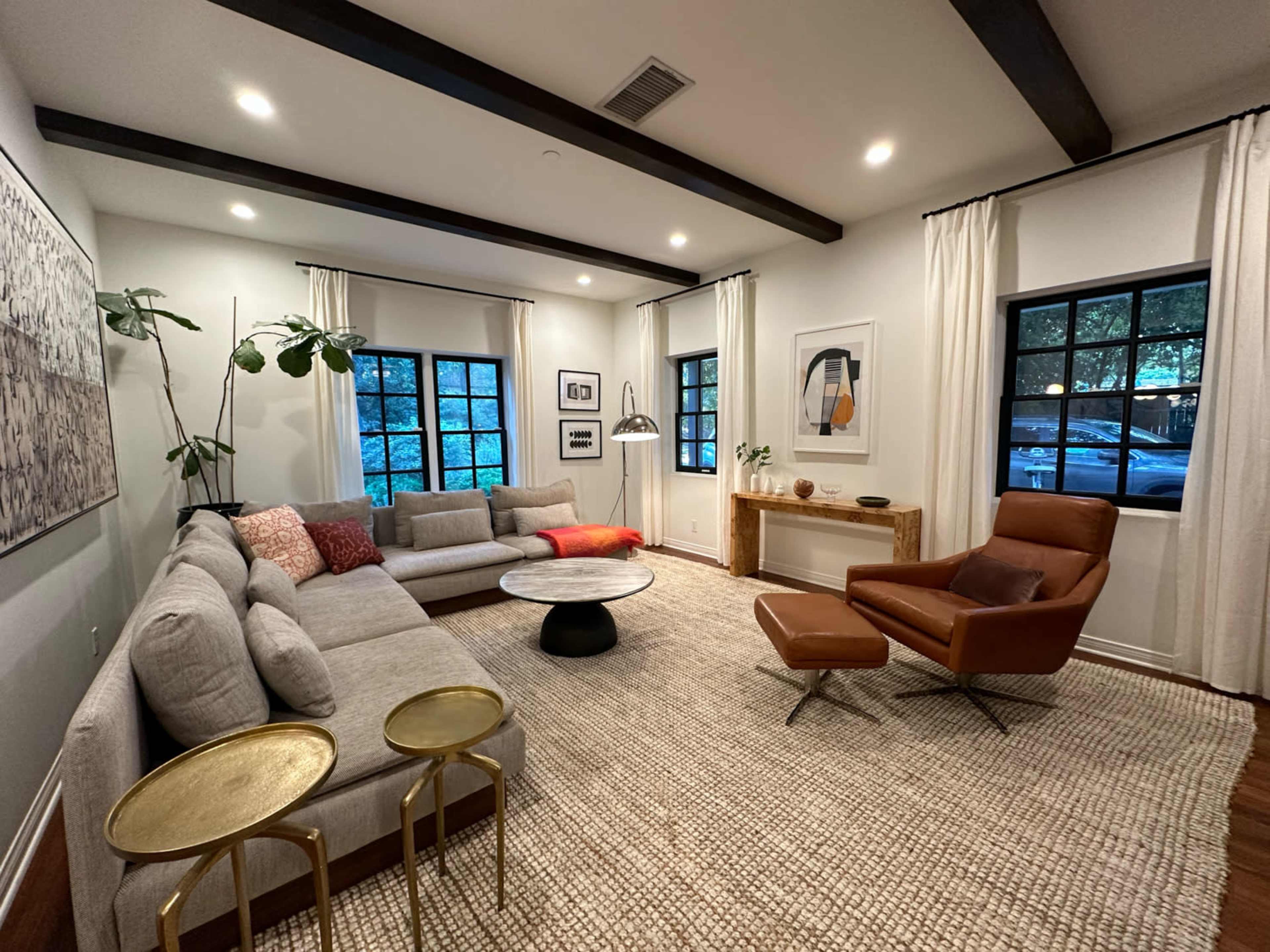A modern living room with a large sectional sofa, an accent chair, a round coffee table, and natural light coming through two windows.