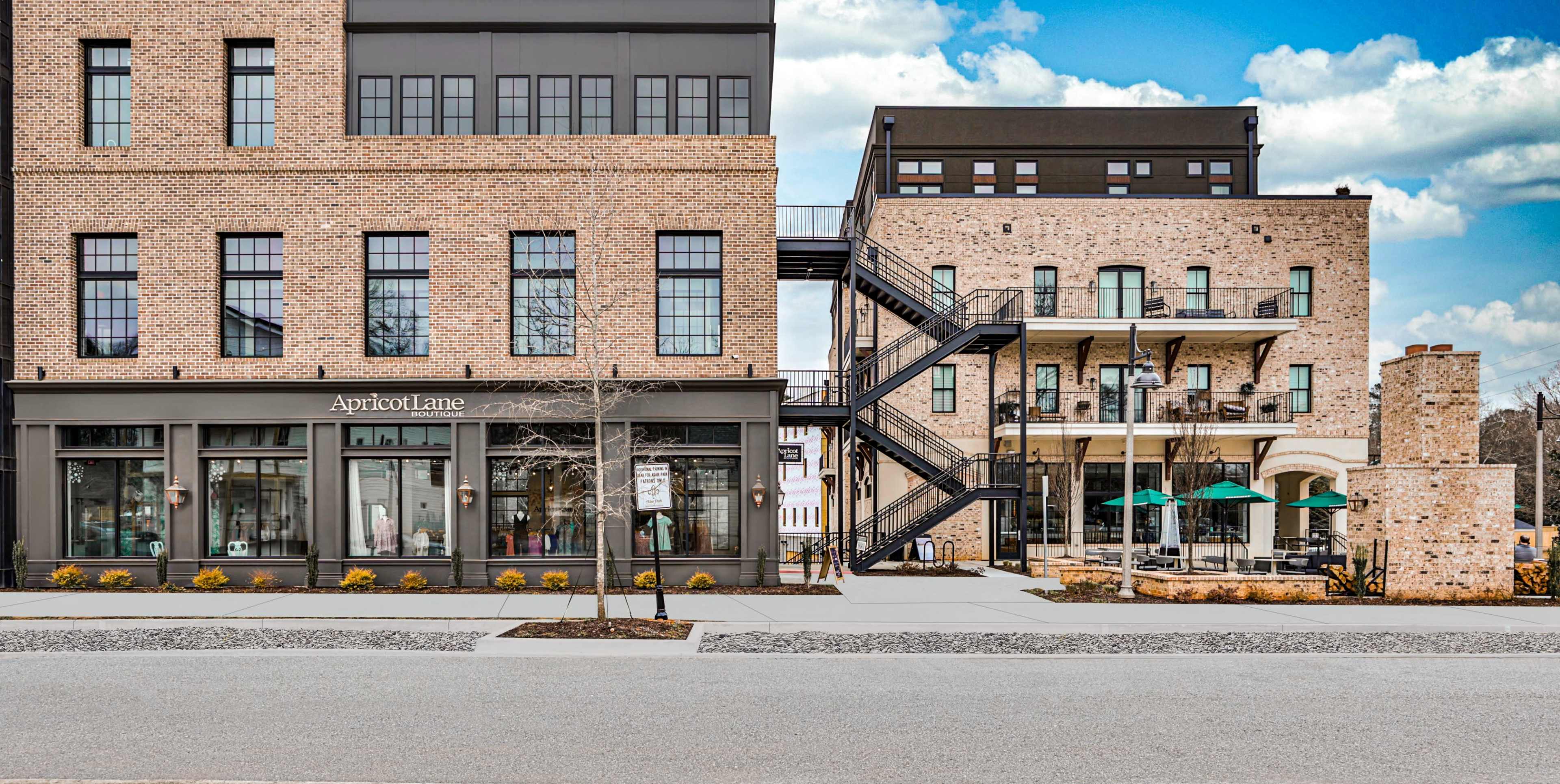 A modern building facade featuring a retail store named "Apricot Lane" on the left and a multi-story residential or commercial building with outdoor seating on the right.