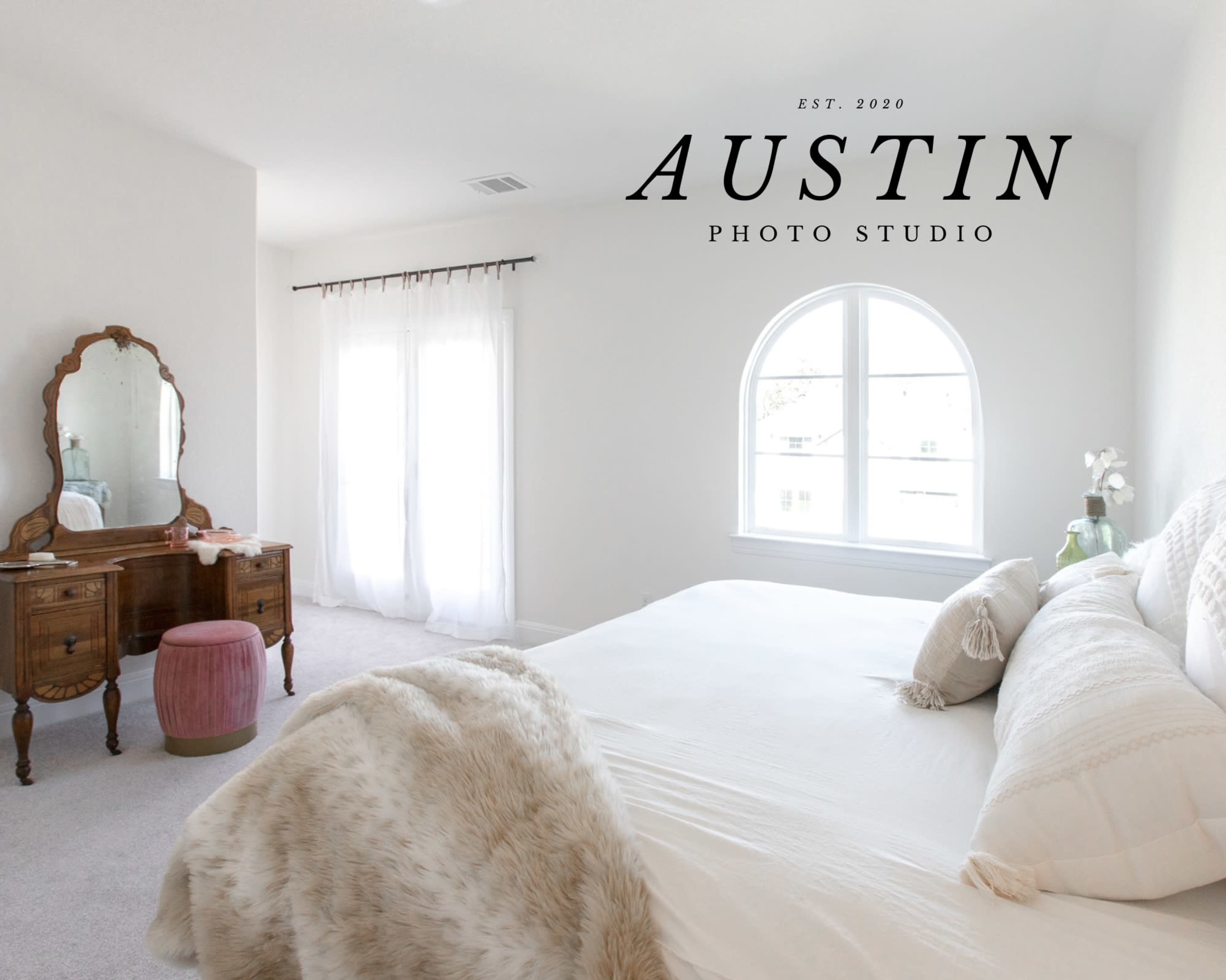 A bright bedroom features a large window, a neatly made bed, a decorative fur throw, and a vintage dresser.