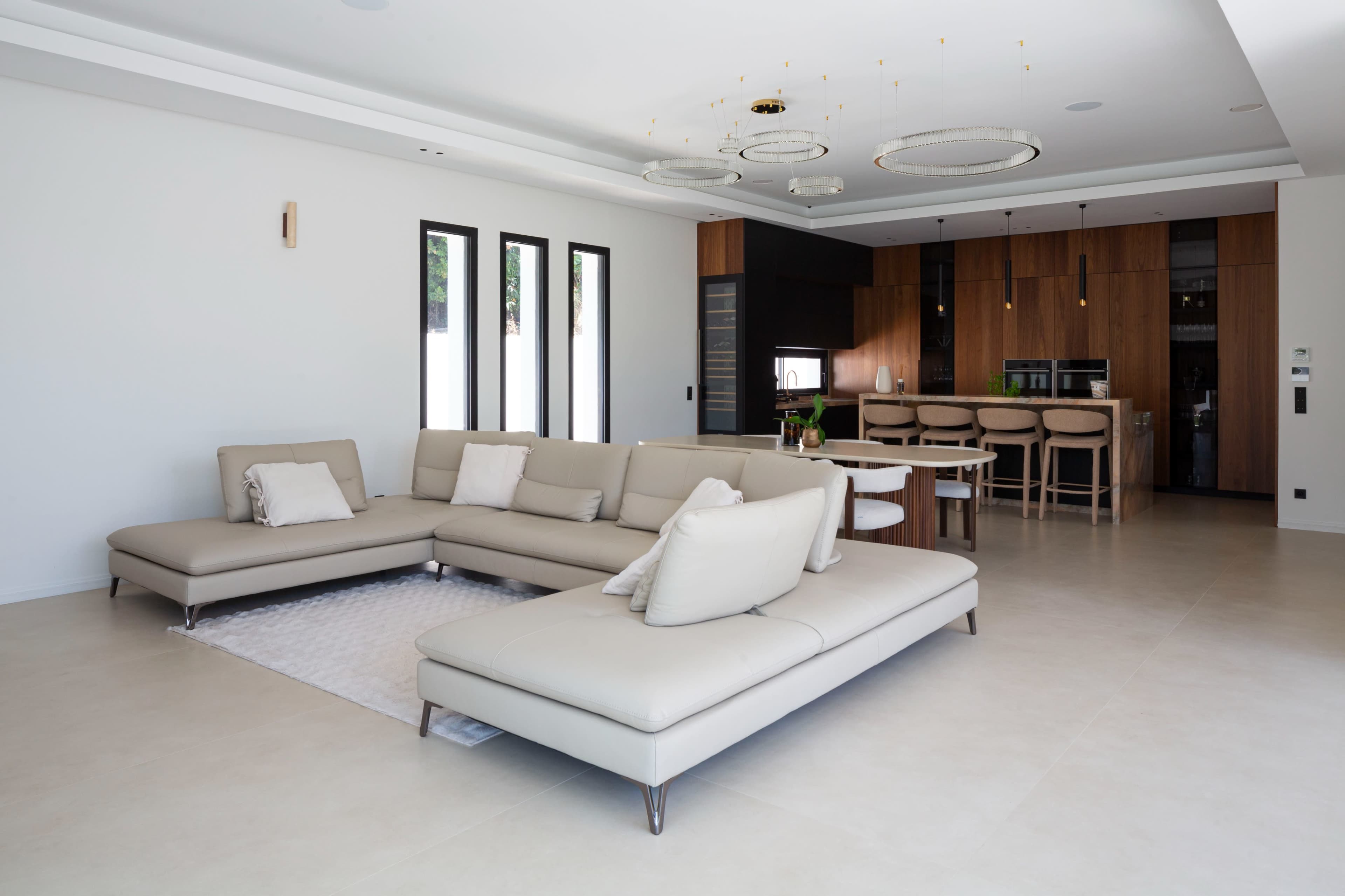 A modern living room features a spacious sectional sofa, a dining table, and wooden cabinetry in the background.
