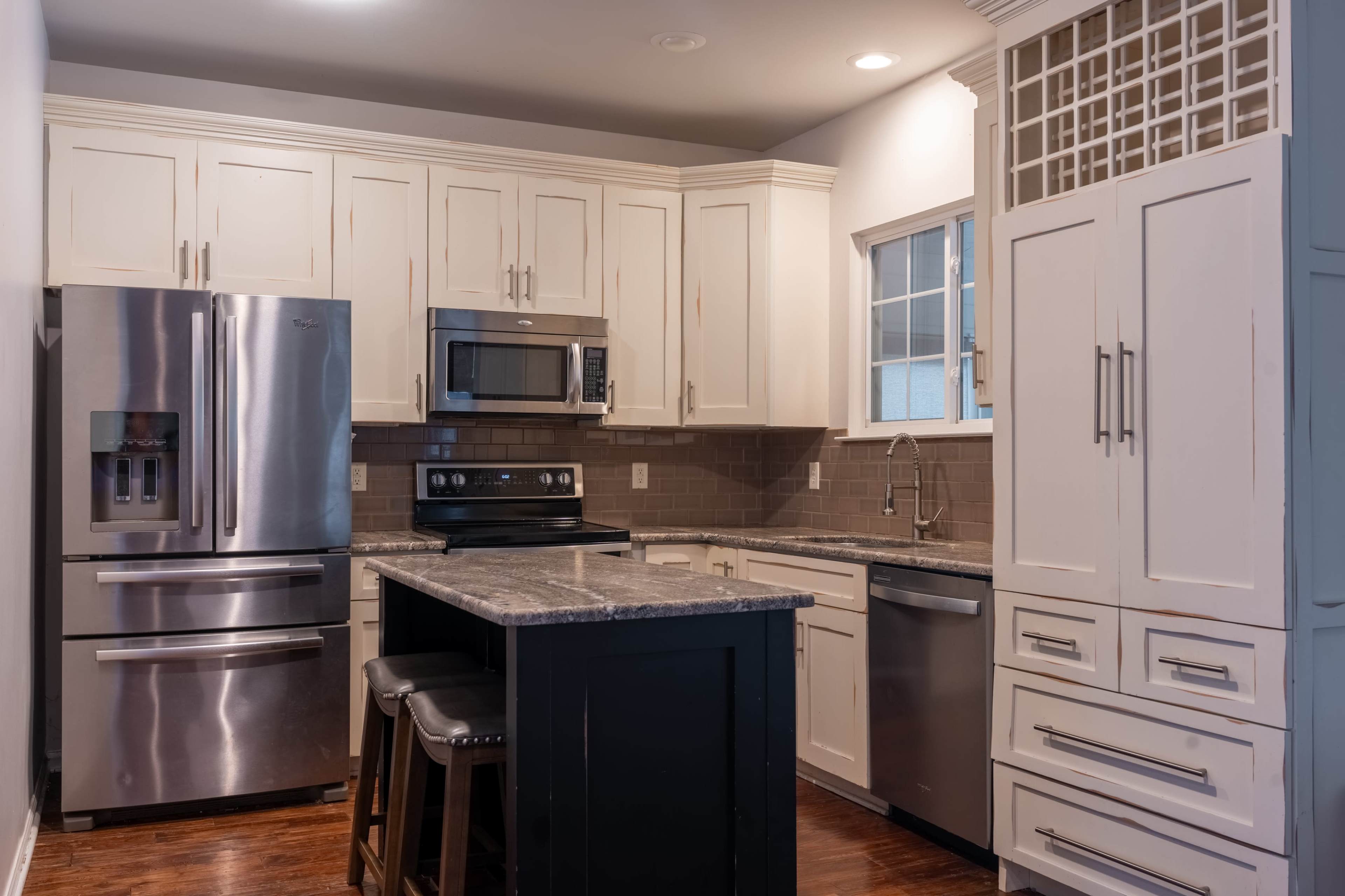 A kitchen with stainless steel appliances, a granite countertop island, and white cabinetry.