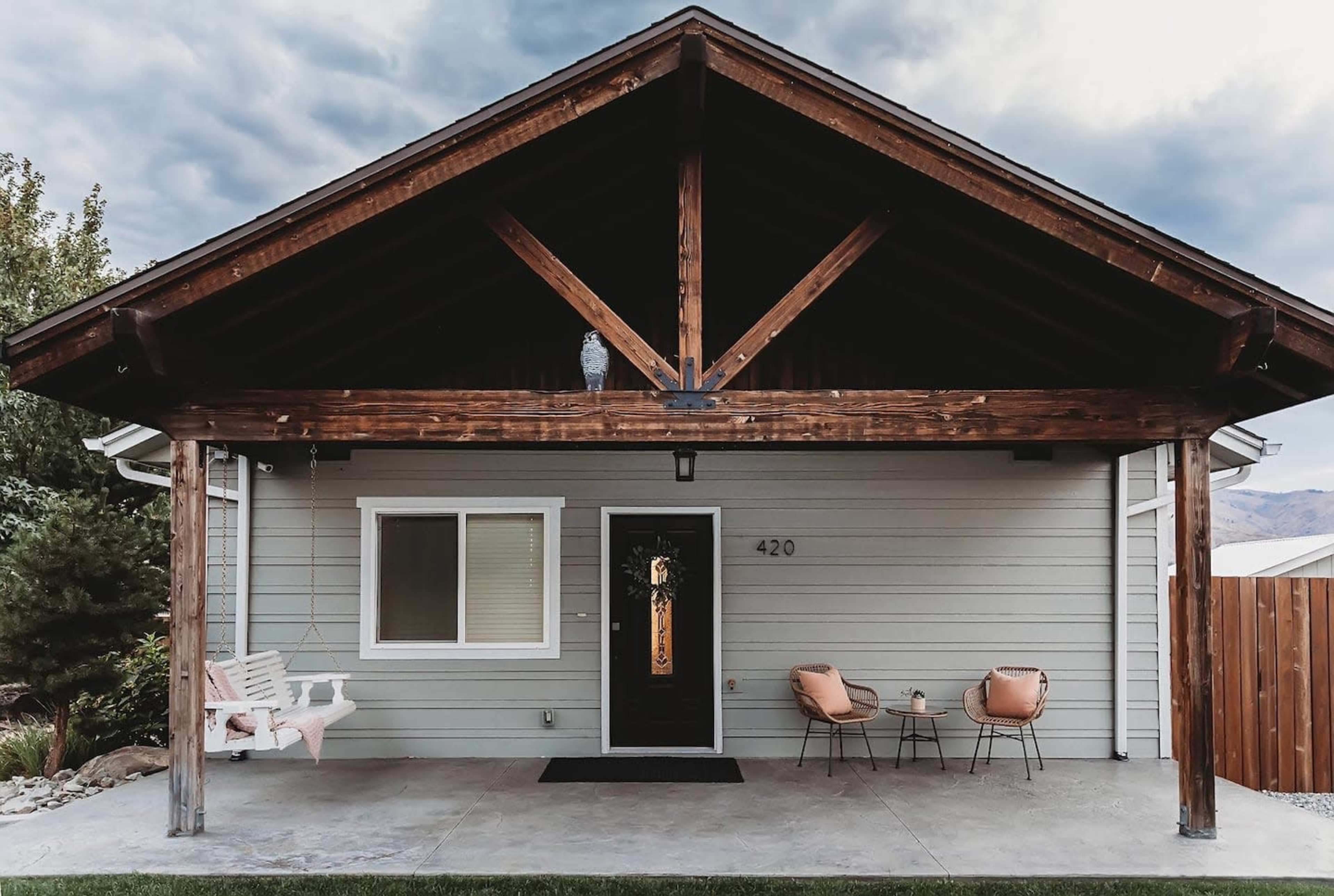 A modern home features a covered porch with two chairs and a swing under a wooden beam structure.