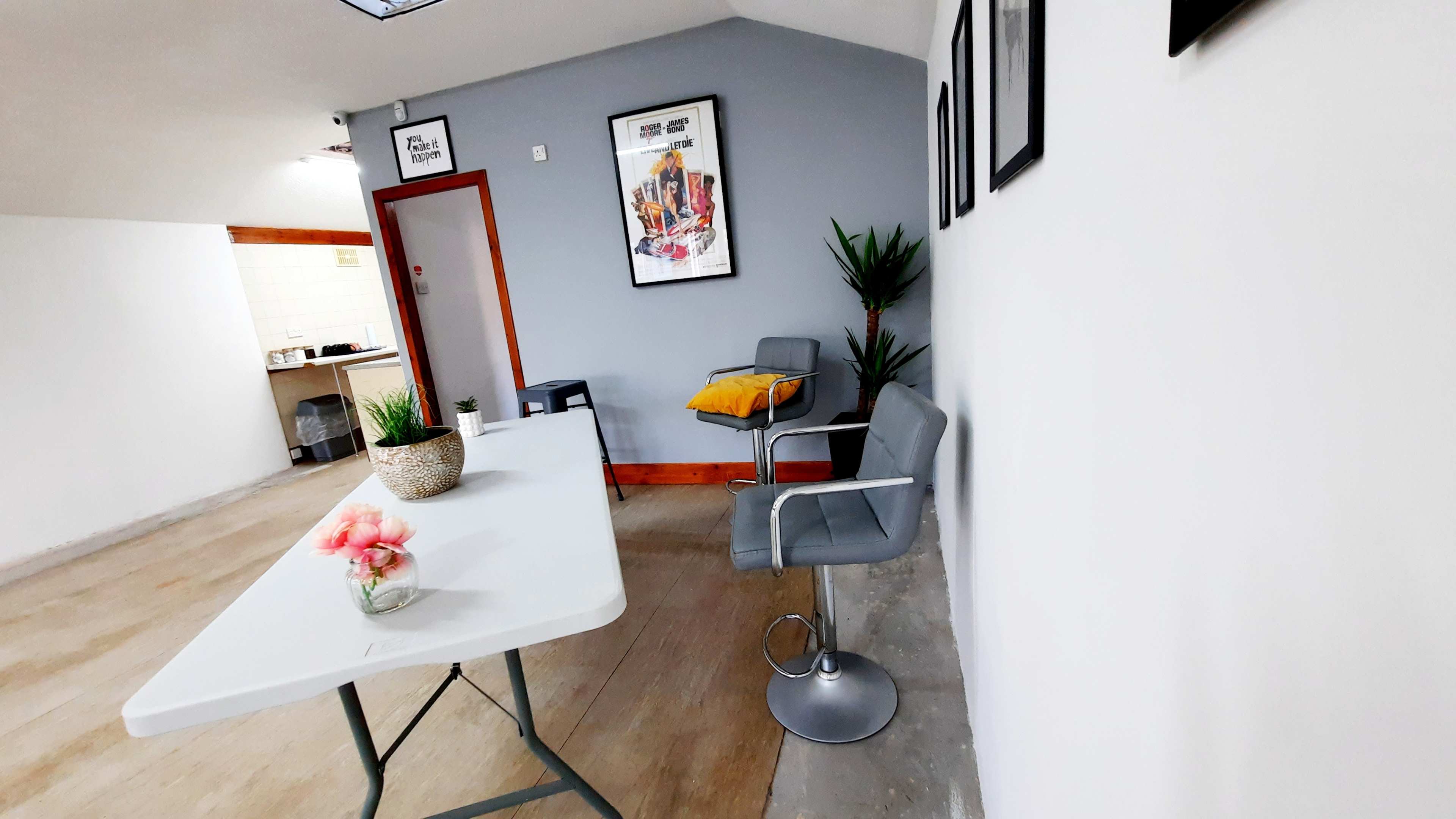 A room with a table, a bar stool, potted plants, and framed artwork on the walls.