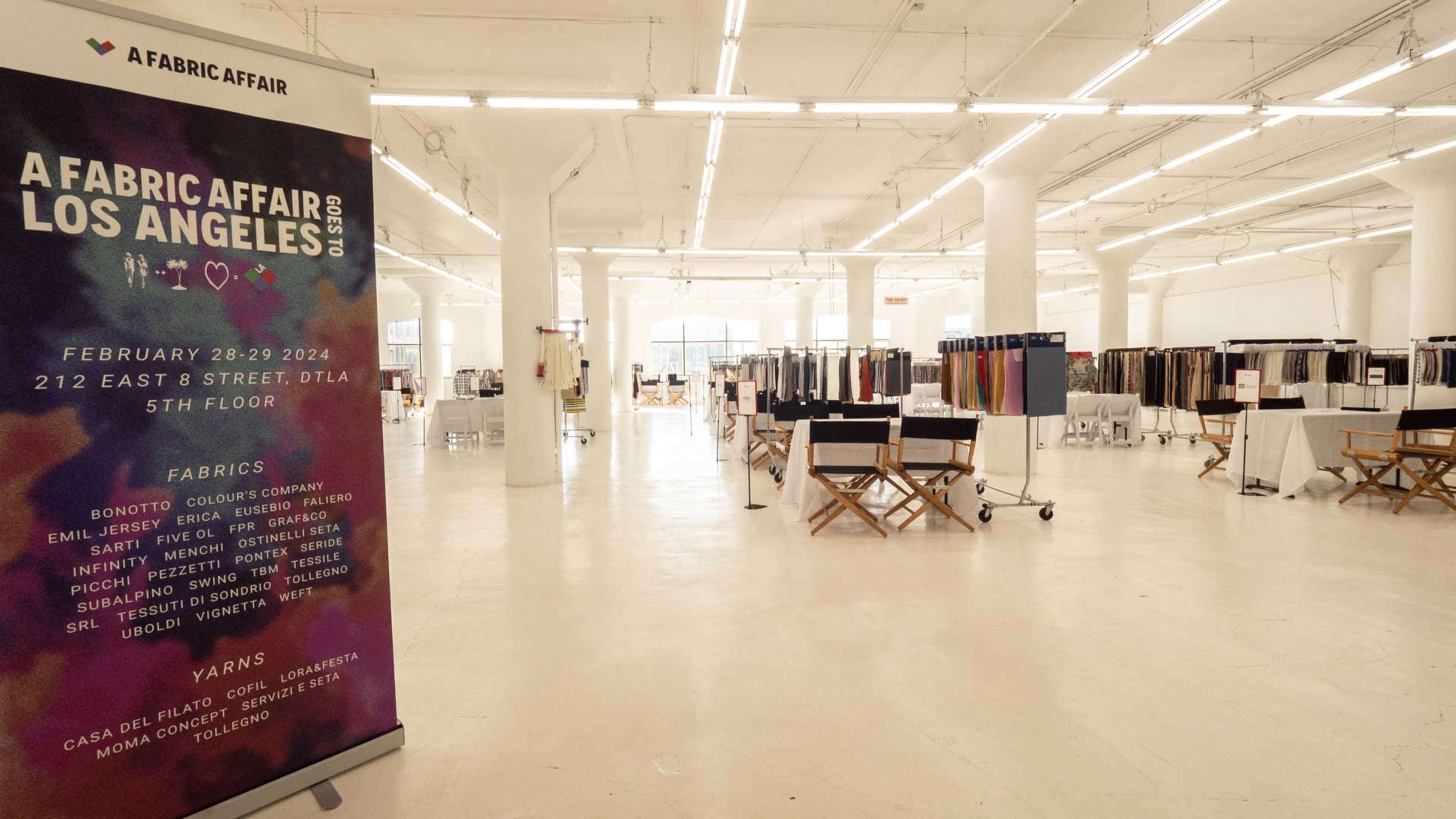 A spacious exhibition area with a large banner for "A Fabric Affair" and numerous fabric displays arranged on stands throughout the room.