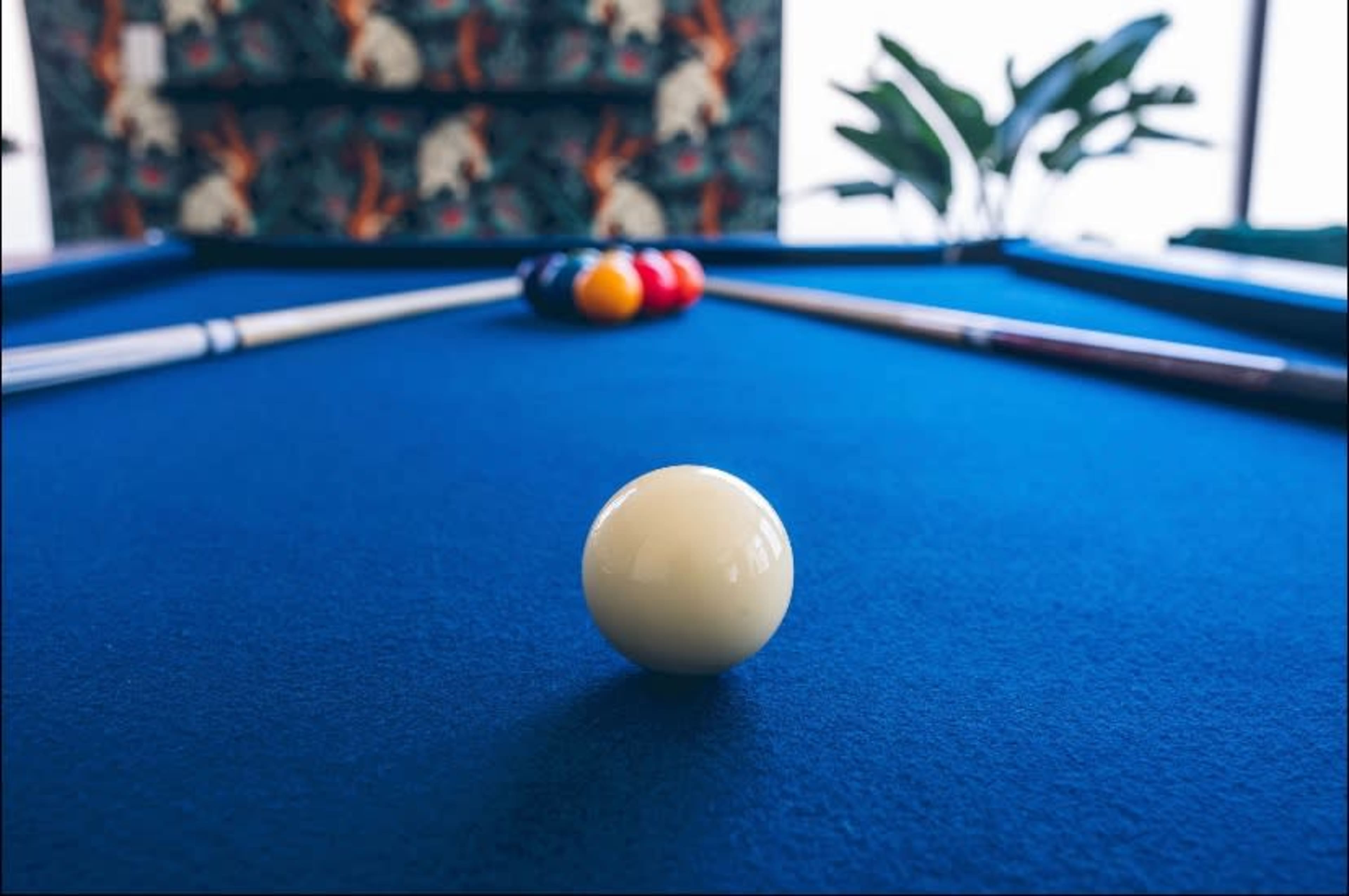 A close-up view of a white billiard ball on a blue table, with a rack of colored balls positioned in the background.
