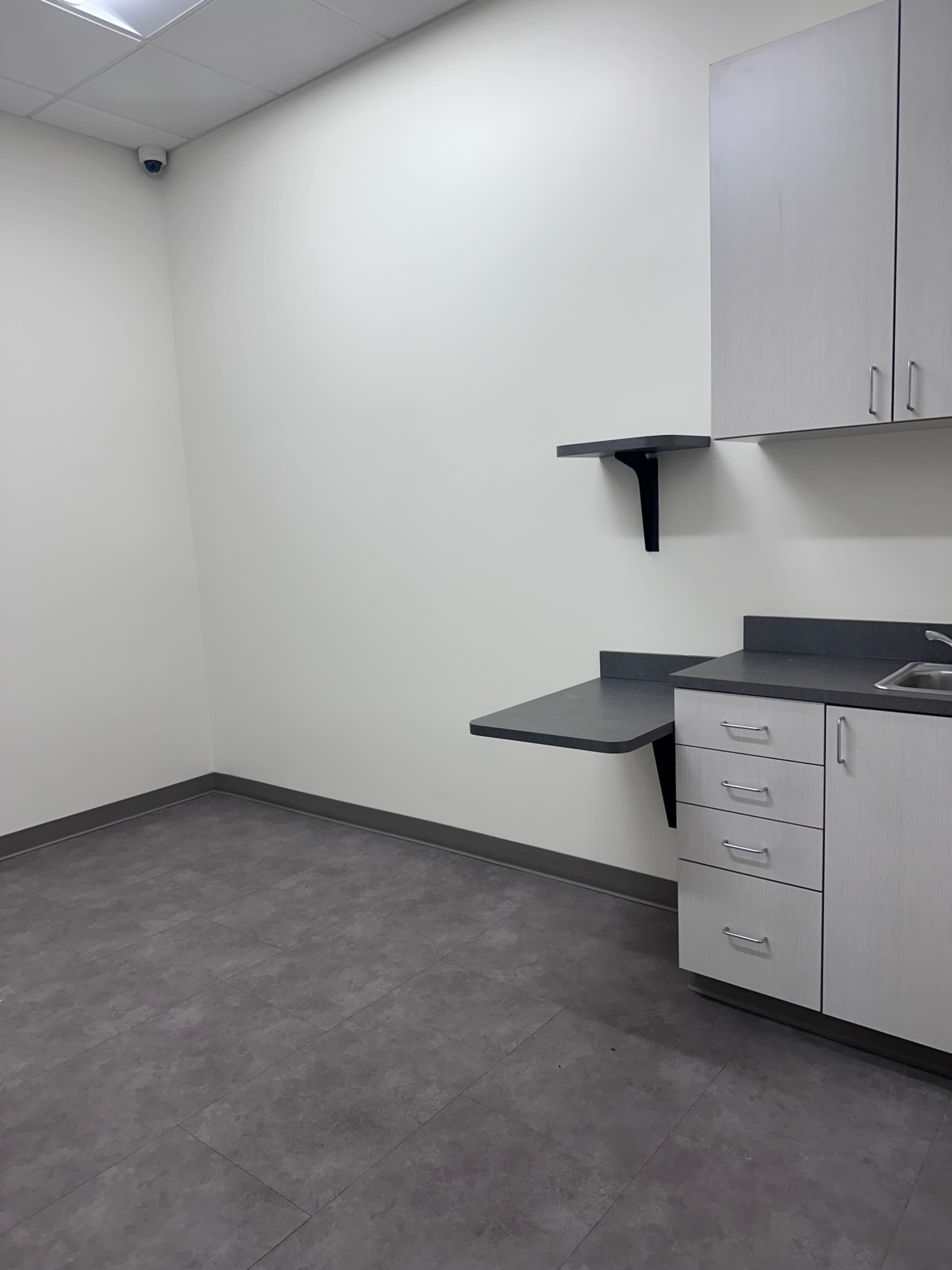 The image shows a small, empty room with light-colored walls, a sink, and a countertop against one side.
