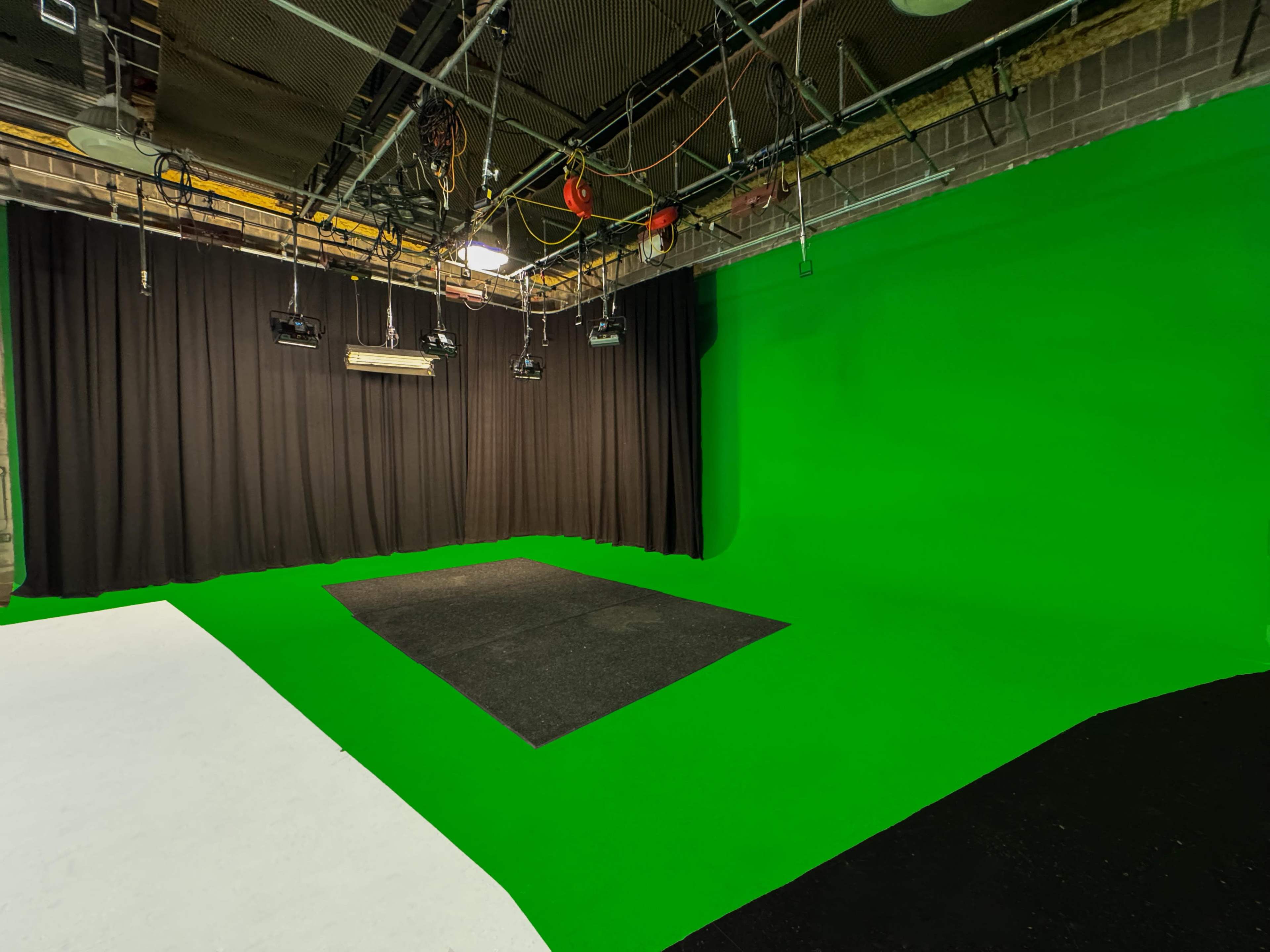 The image shows a green screen studio with a black curtain backdrop and a textured floor area.