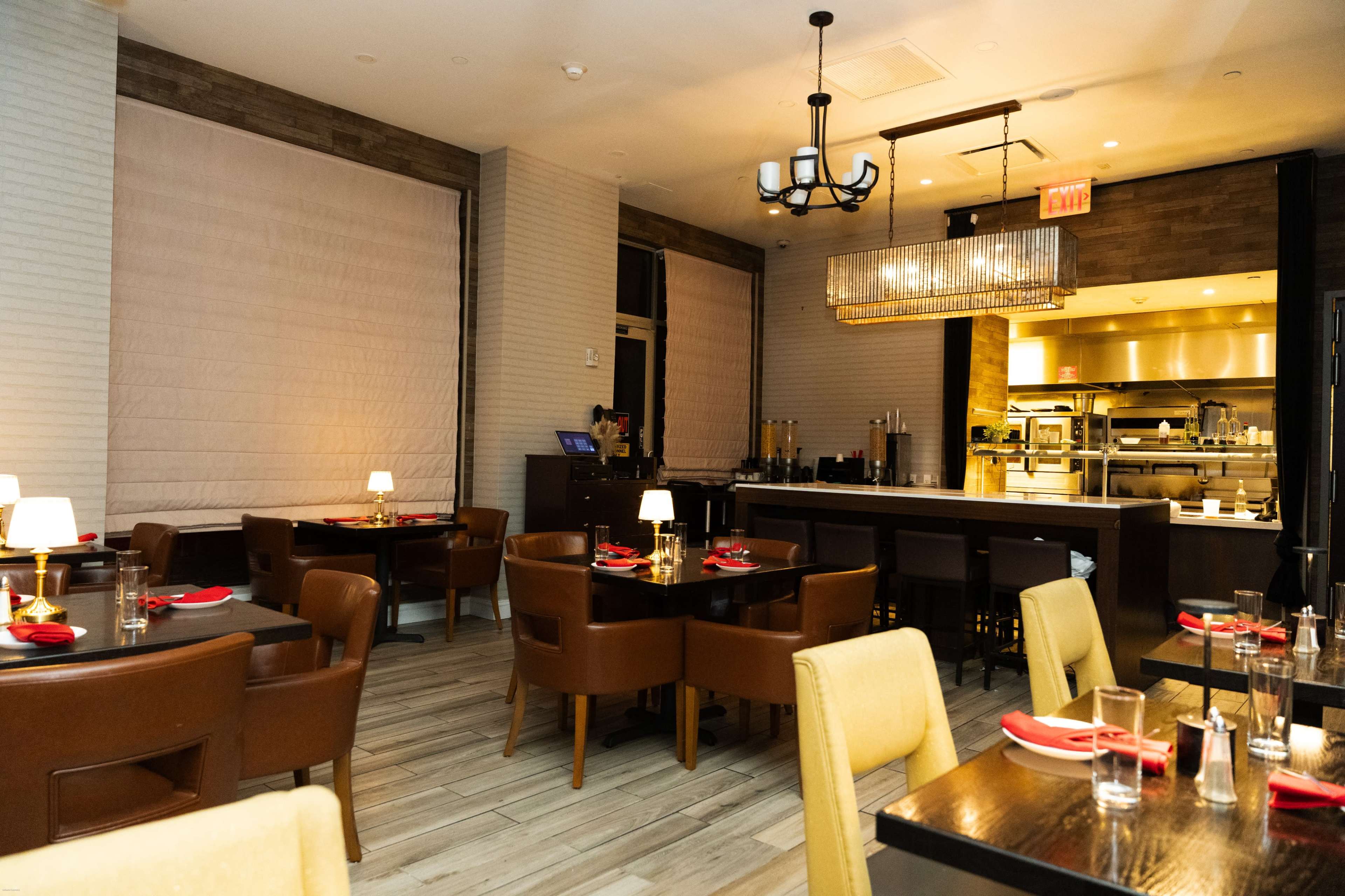 The image shows an upscale restaurant interior featuring wooden tables, leather chairs, and a kitchen area visible in the background.
