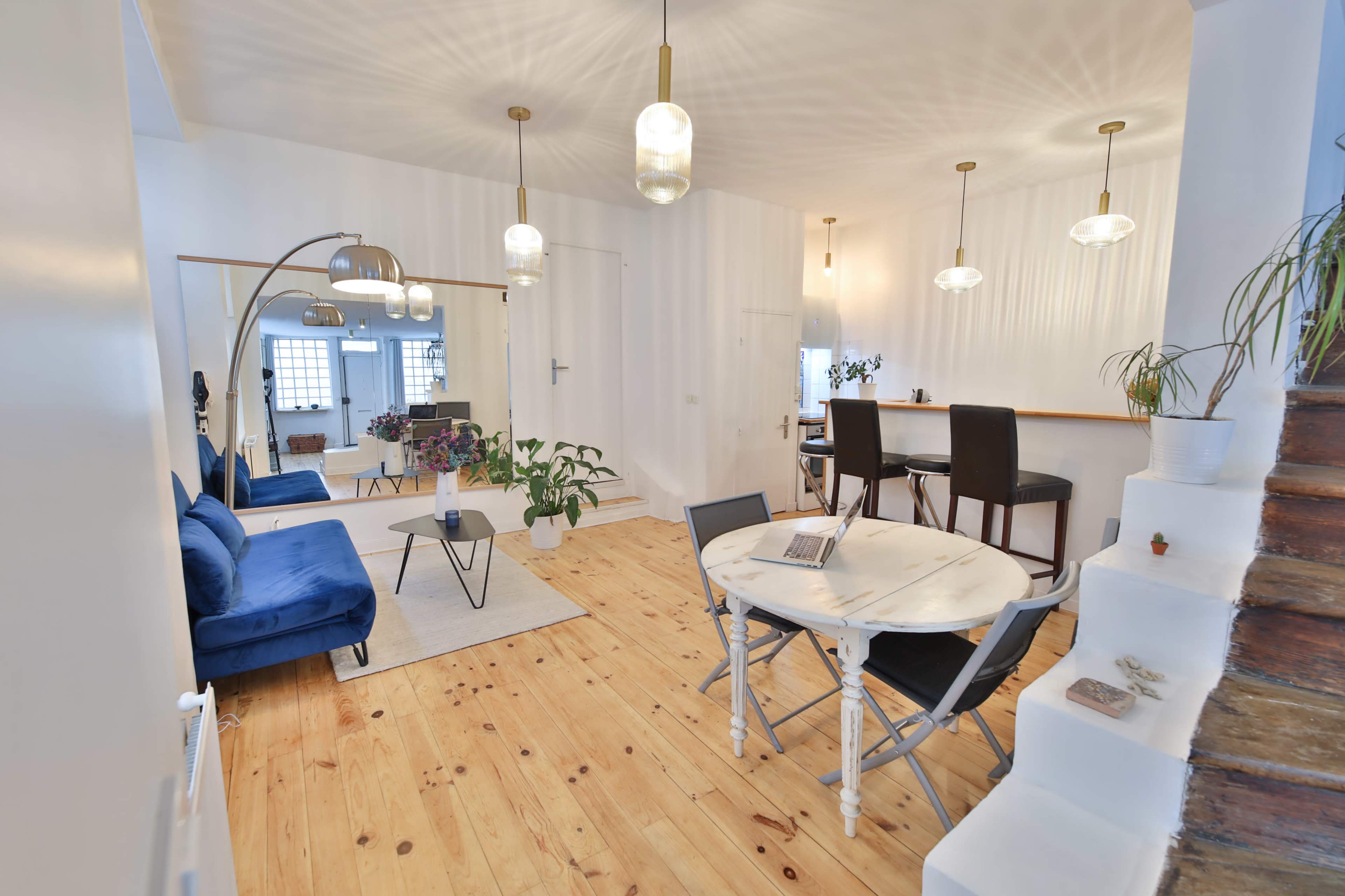 A bright, open living room and dining area featuring a blue sofa, a round dining table, and pendant lighting.
