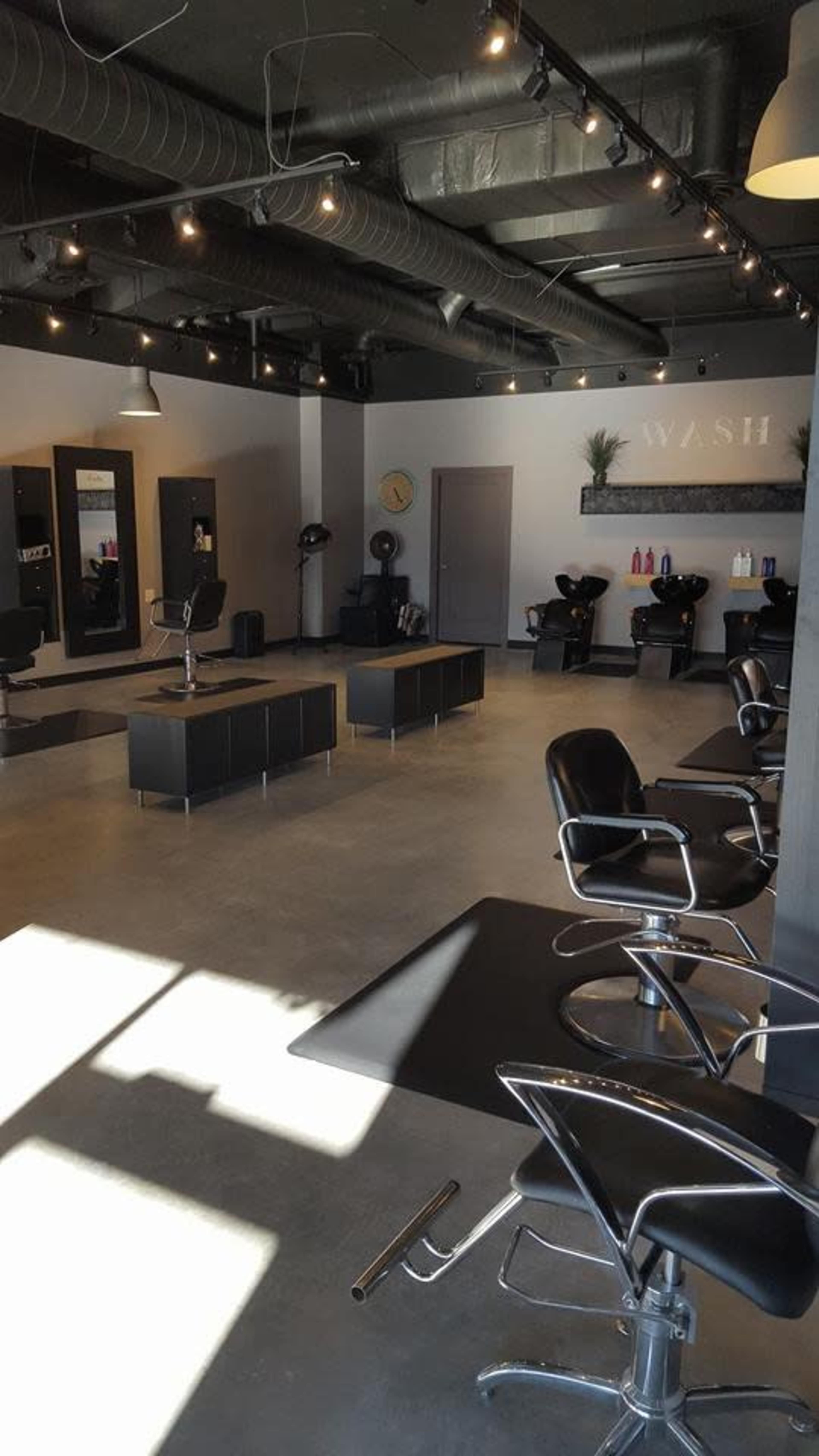 The image shows a modern hair salon with styling chairs, wash stations, and mirrors under soft lighting.