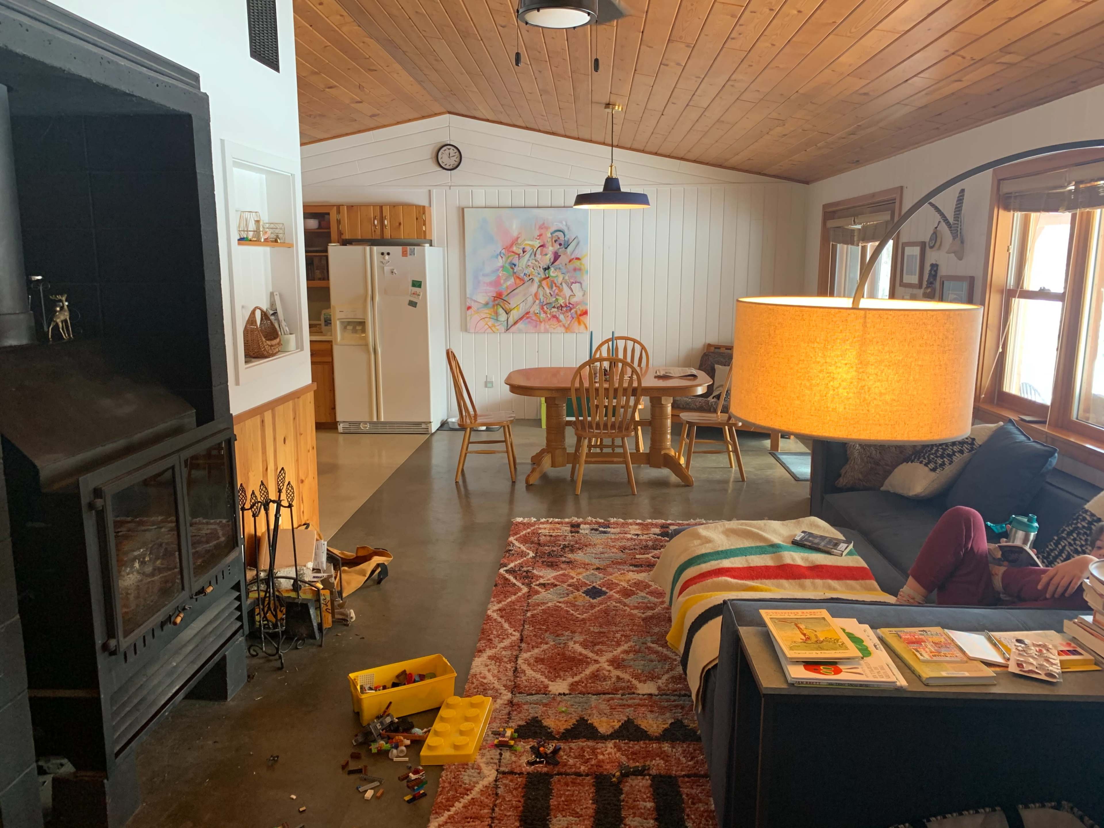 A cozy living space features a fireplace, a dining area, and a couch with a large lamp, showcasing a mix of furniture and colorful decor.