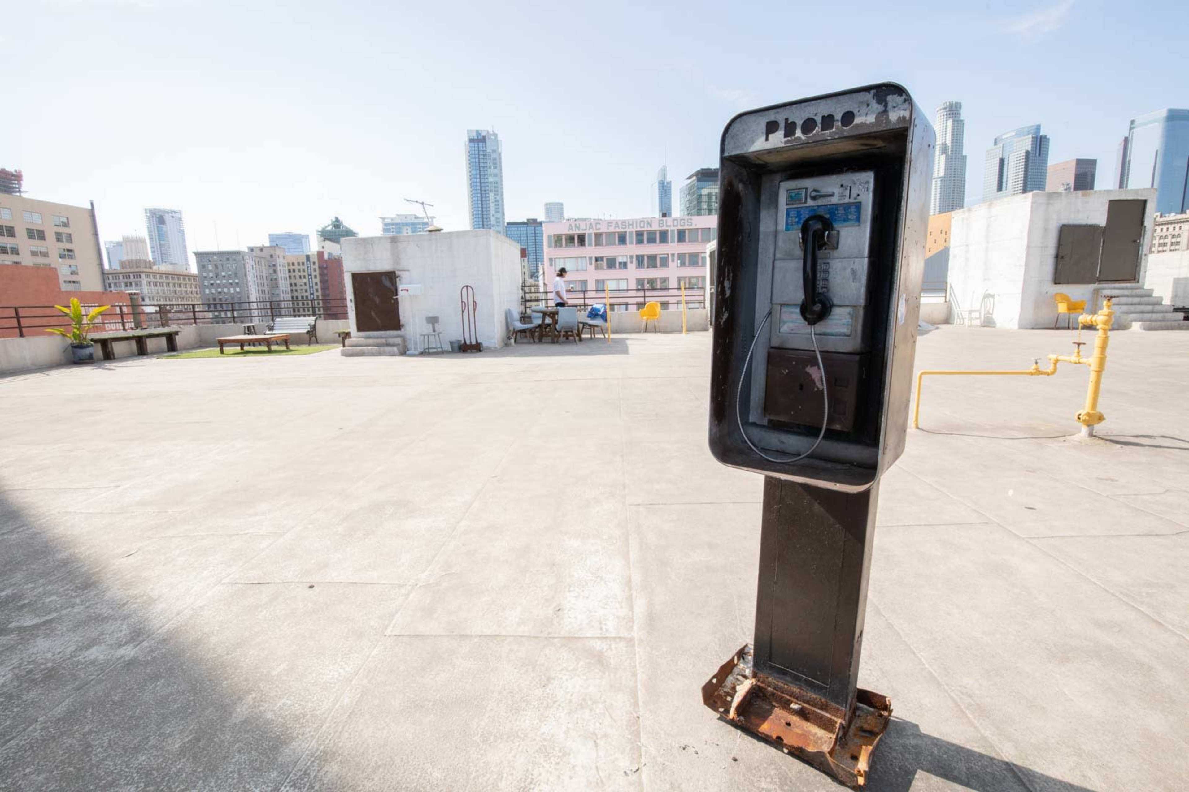 A payphone stands on a rooftop surrounded by city skyscrapers in the background.
