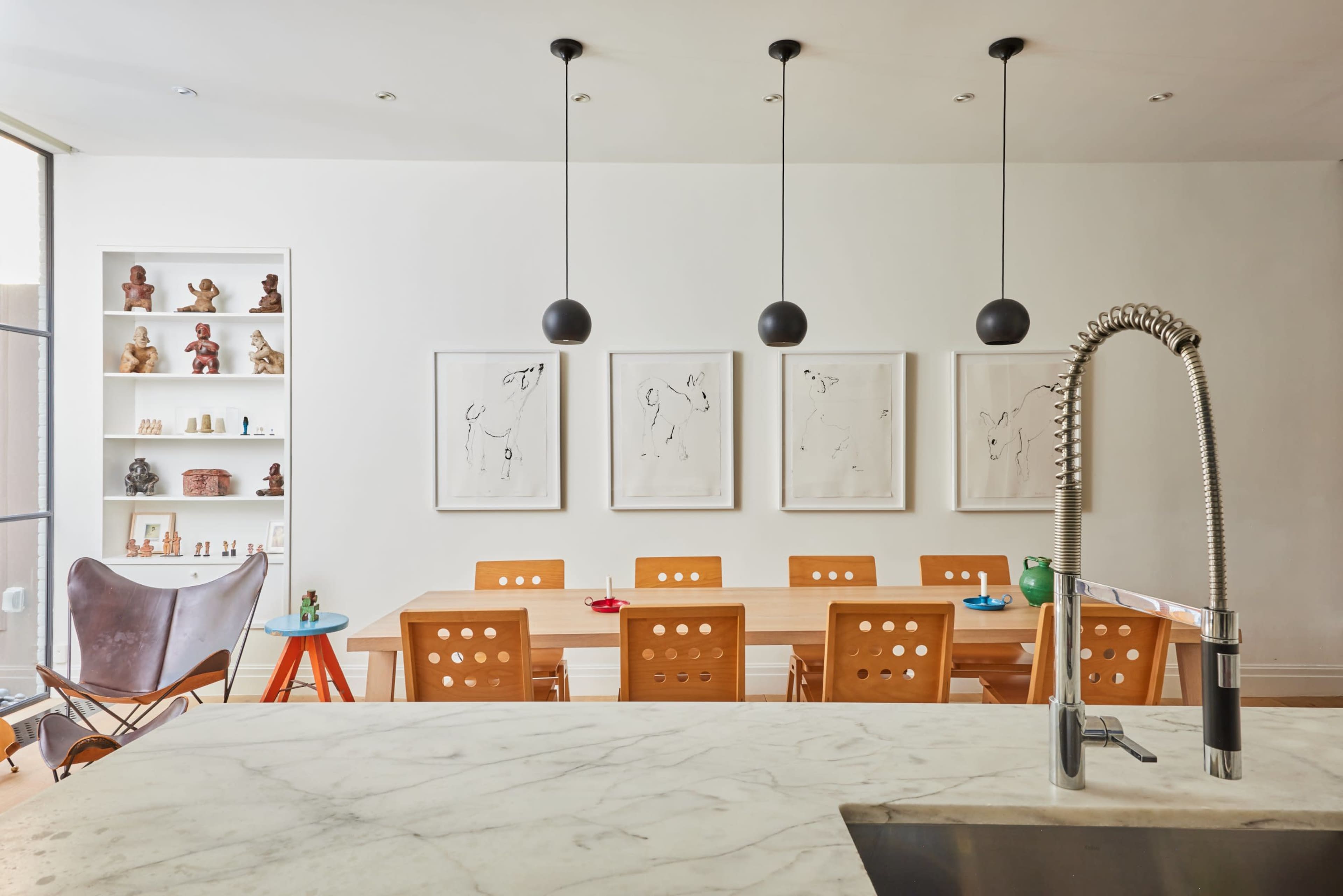 A modern kitchen features a marble countertop, a sleek faucet, and a dining table with eight wooden chairs facing three framed artworks on the wall.