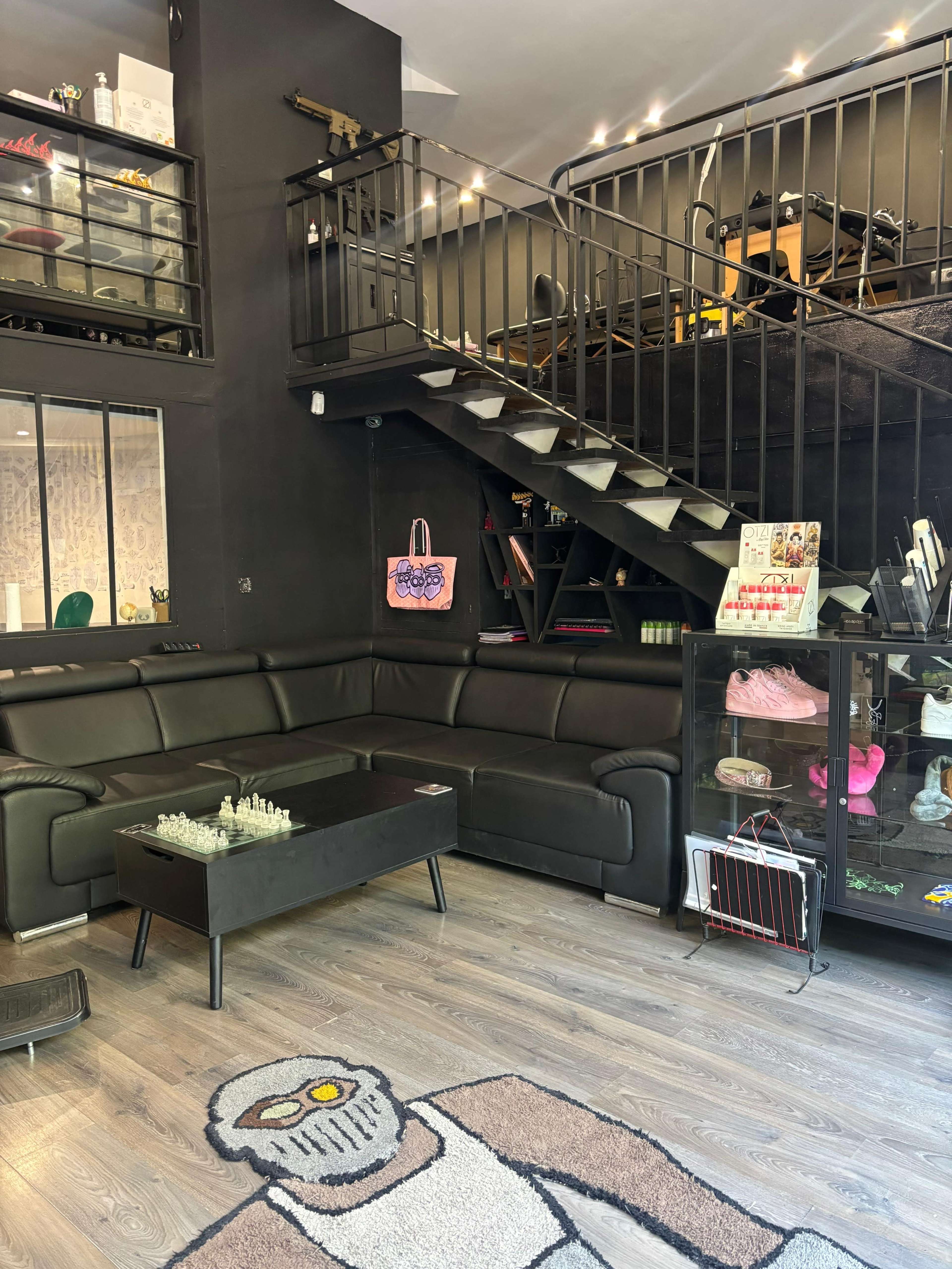 The image shows a modern interior of a lounge area featuring a large black sectional sofa, a coffee table, and a staircase leading to an upper level.