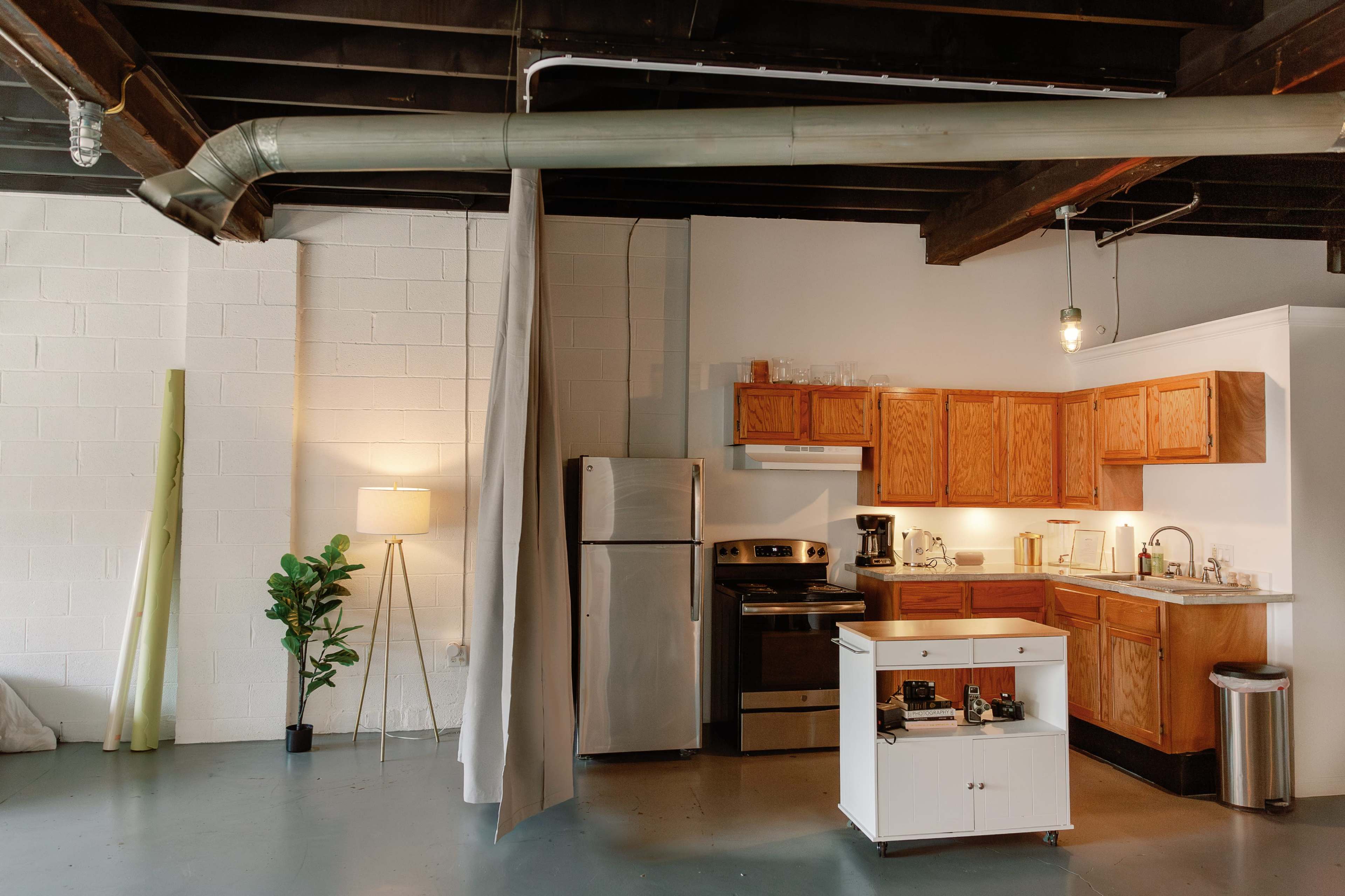 The image shows a modern kitchen area within a spacious loft featuring wooden cabinets, stainless steel appliances, and a small island.