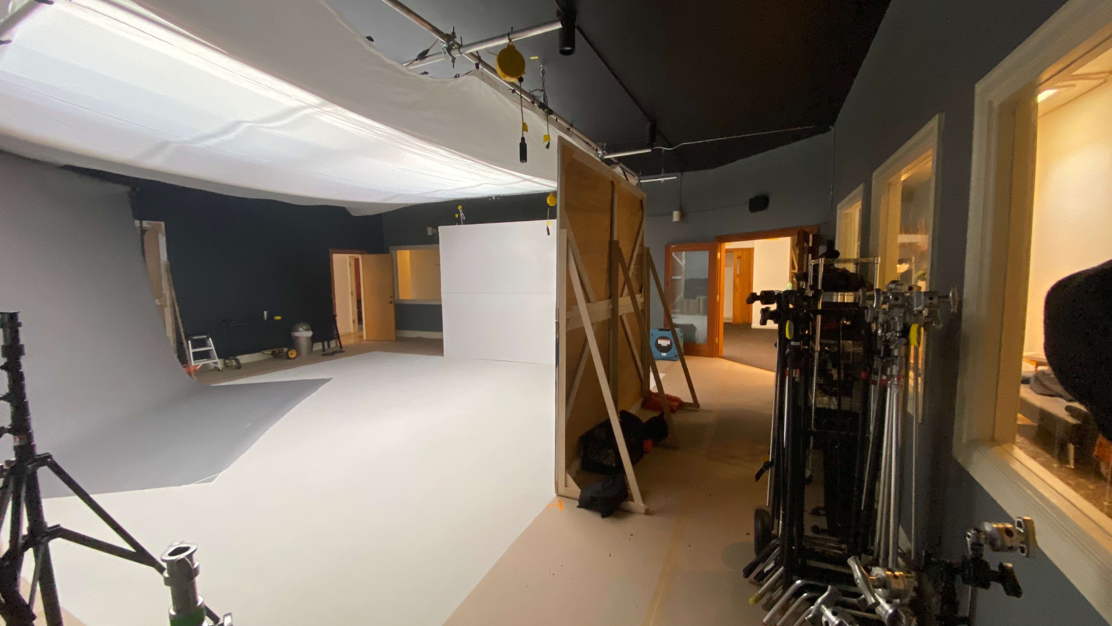 A photography studio with a large, empty shooting area, a white backdrop, and equipment stored on the side.