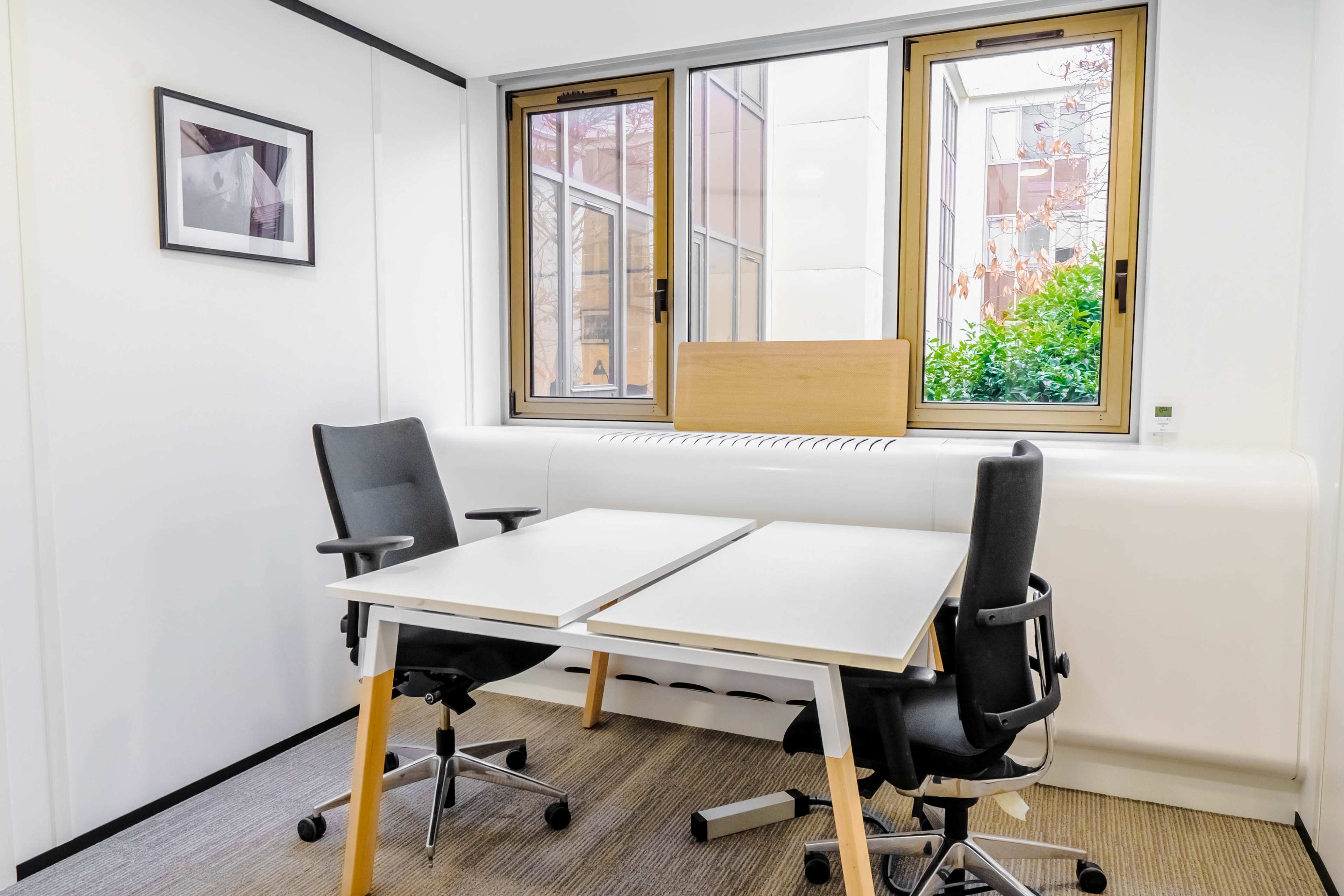 The image shows a small office space with two chairs and a double desk positioned next to large windows.
