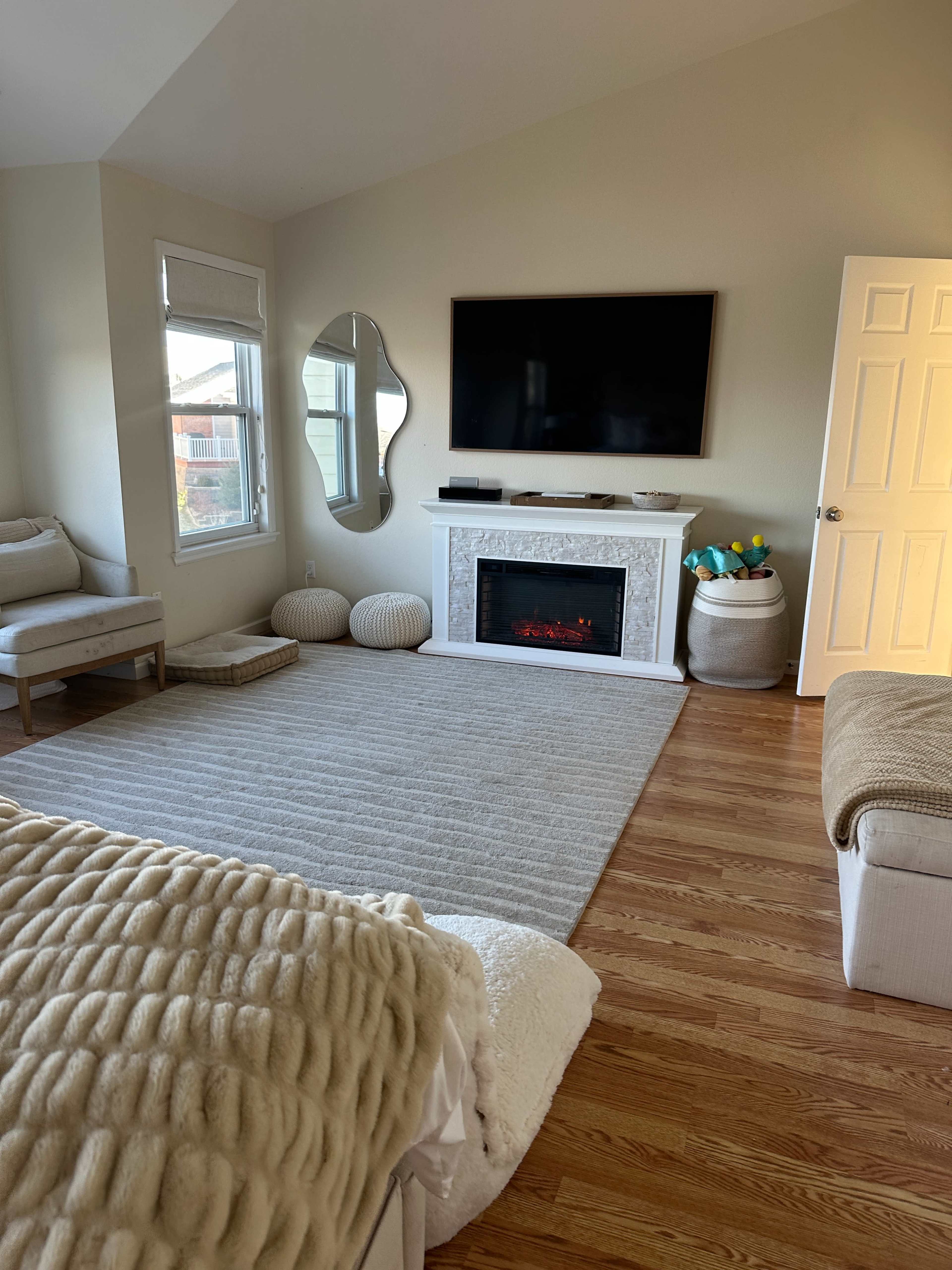 The living room features a large flat-screen TV mounted on the wall above a white fireplace, with a light-colored rug covering the wooden floor.