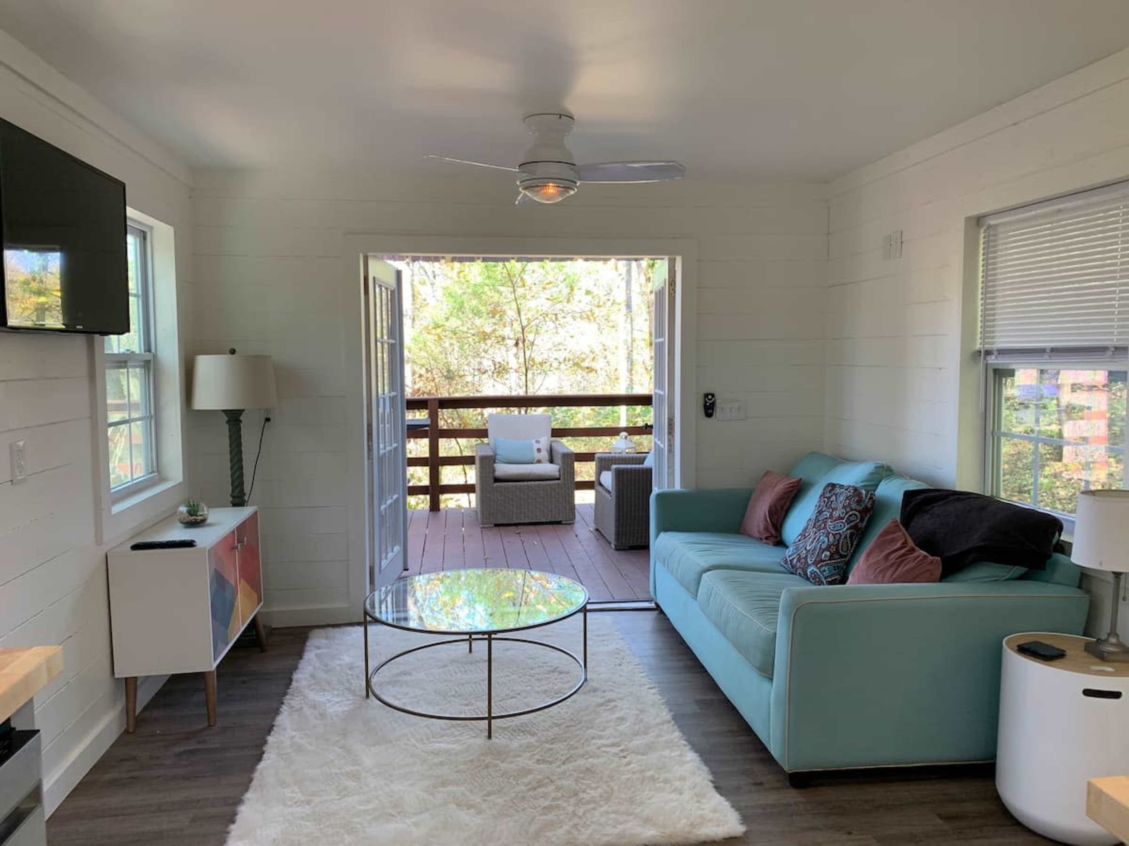A cozy living room with a light blue couch, a round coffee table on a white rug, and sliding doors leading to a deck.